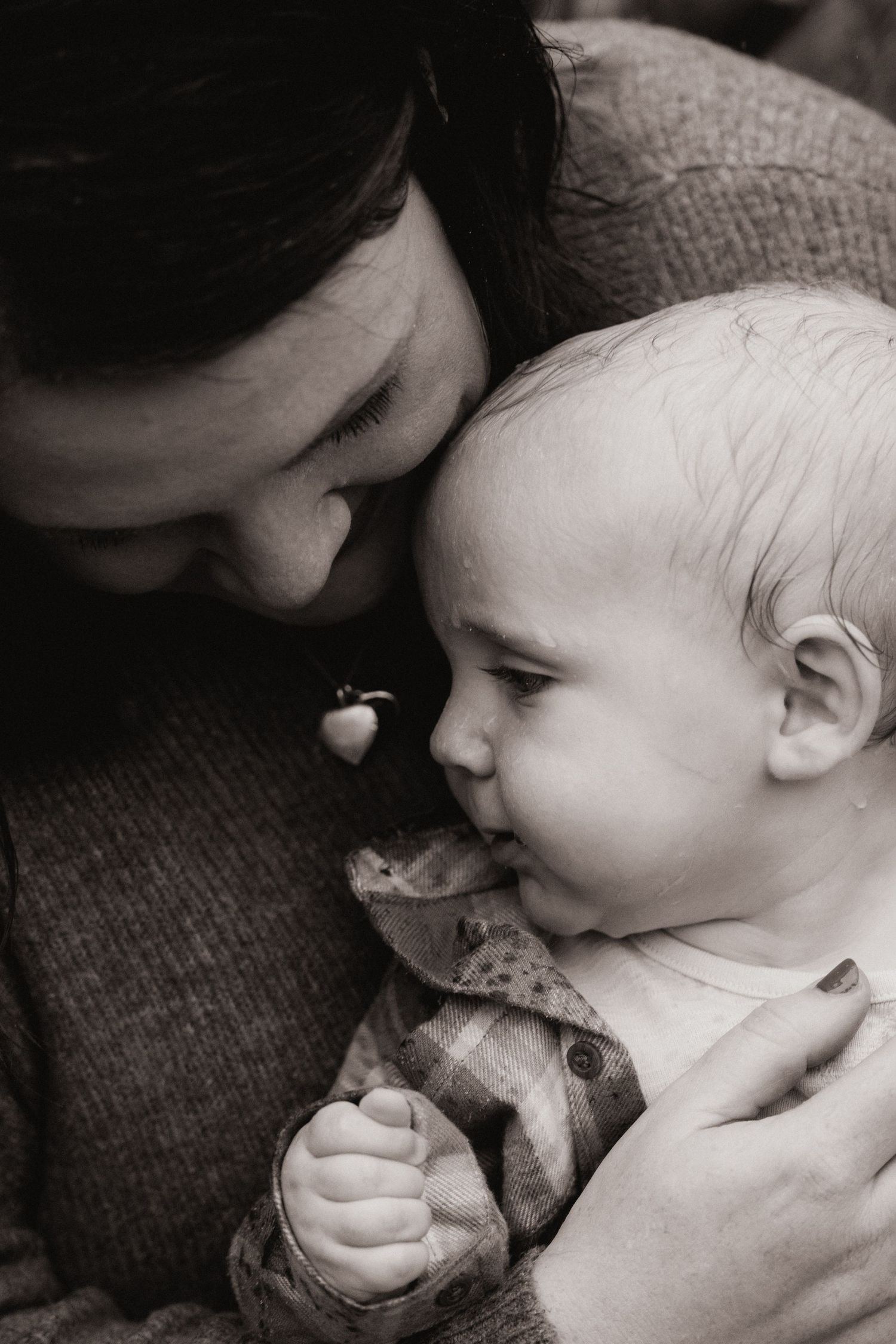 Mother holds her baby close, sharing a soft, tender moment in natural light.