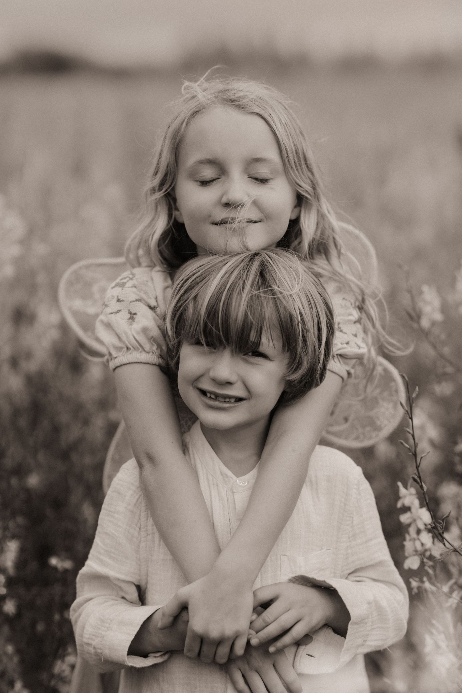 Two siblings hugging in a wildflower meadow during a gentle documentary family photoshoot.