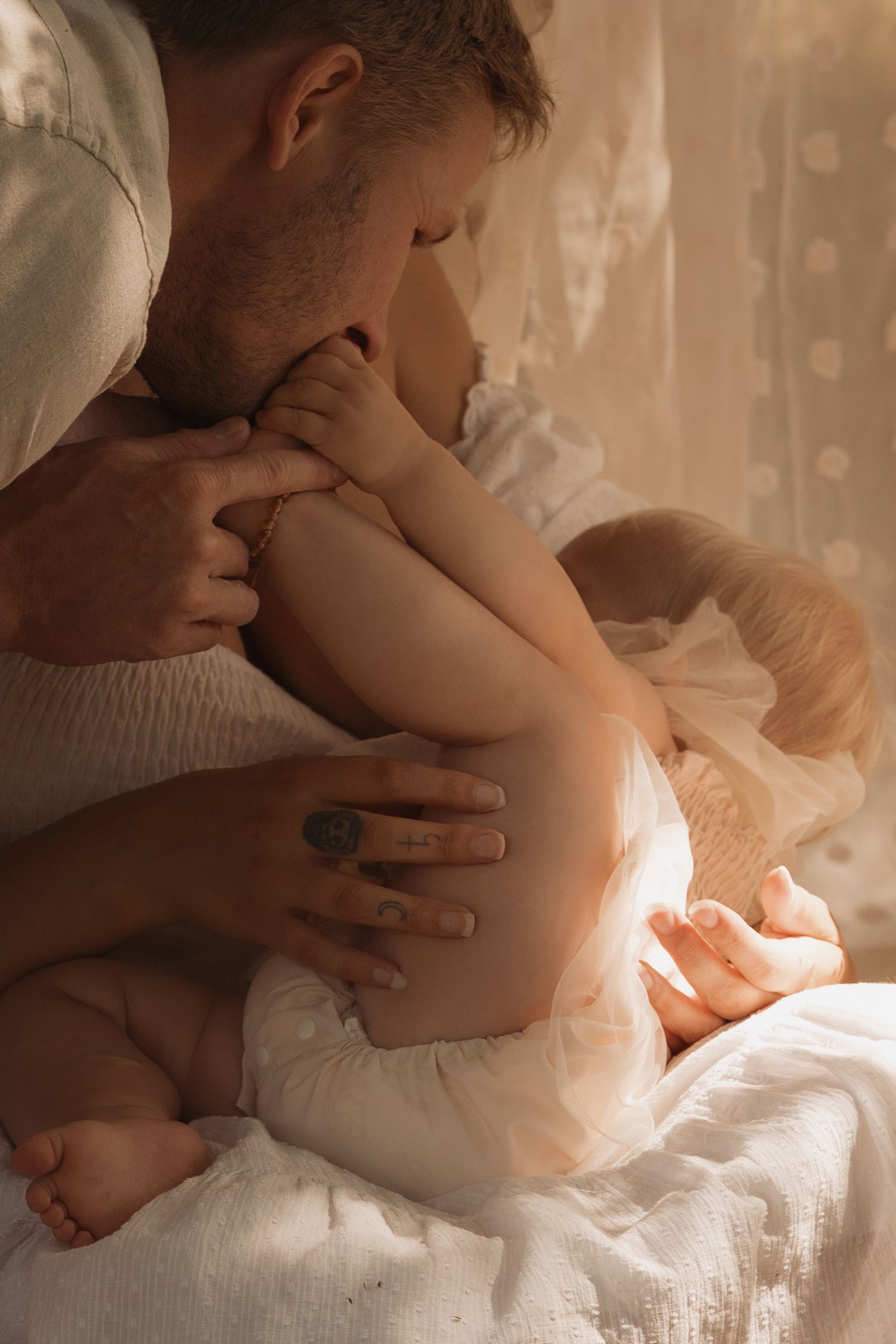 Father kissing his baby’s feet in soft window light during an intimate first birthday photoshoot in Burton on Trent