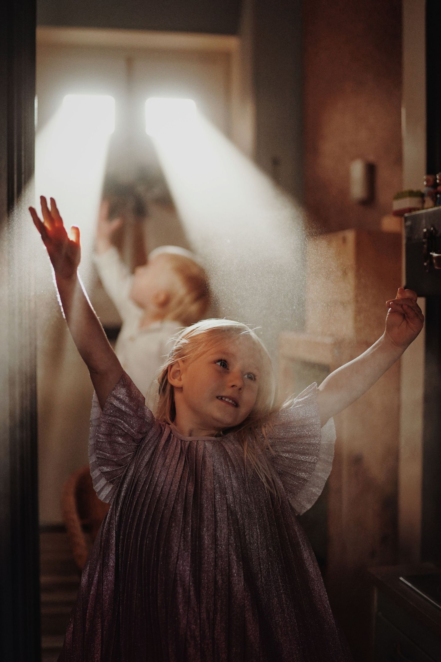 Little girl reaches for light beams in a soft, magical childhood photography session at home.