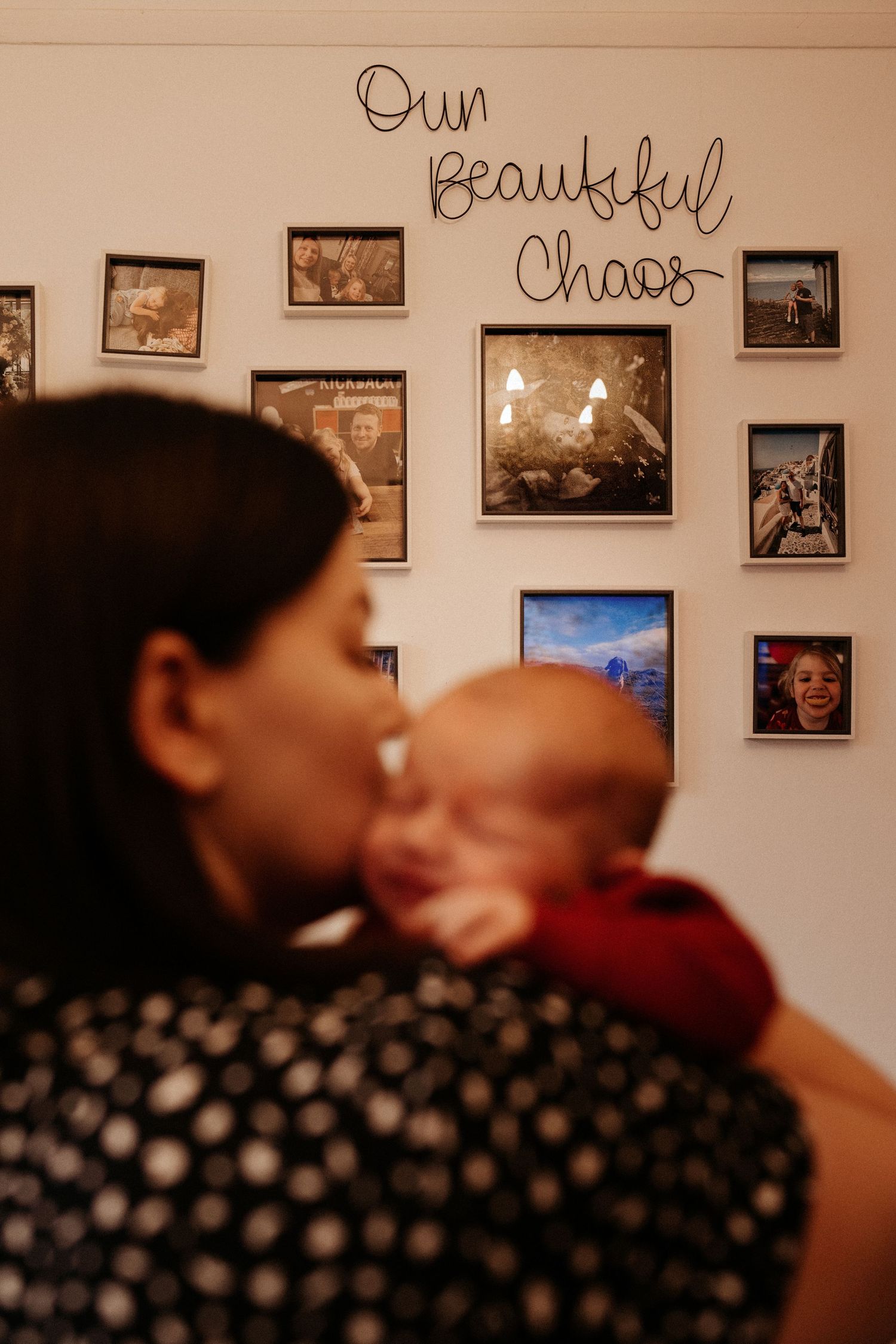 Mother holding her baby at home beneath family photos during a relaxed lifestyle newborn photoshoot in woodville