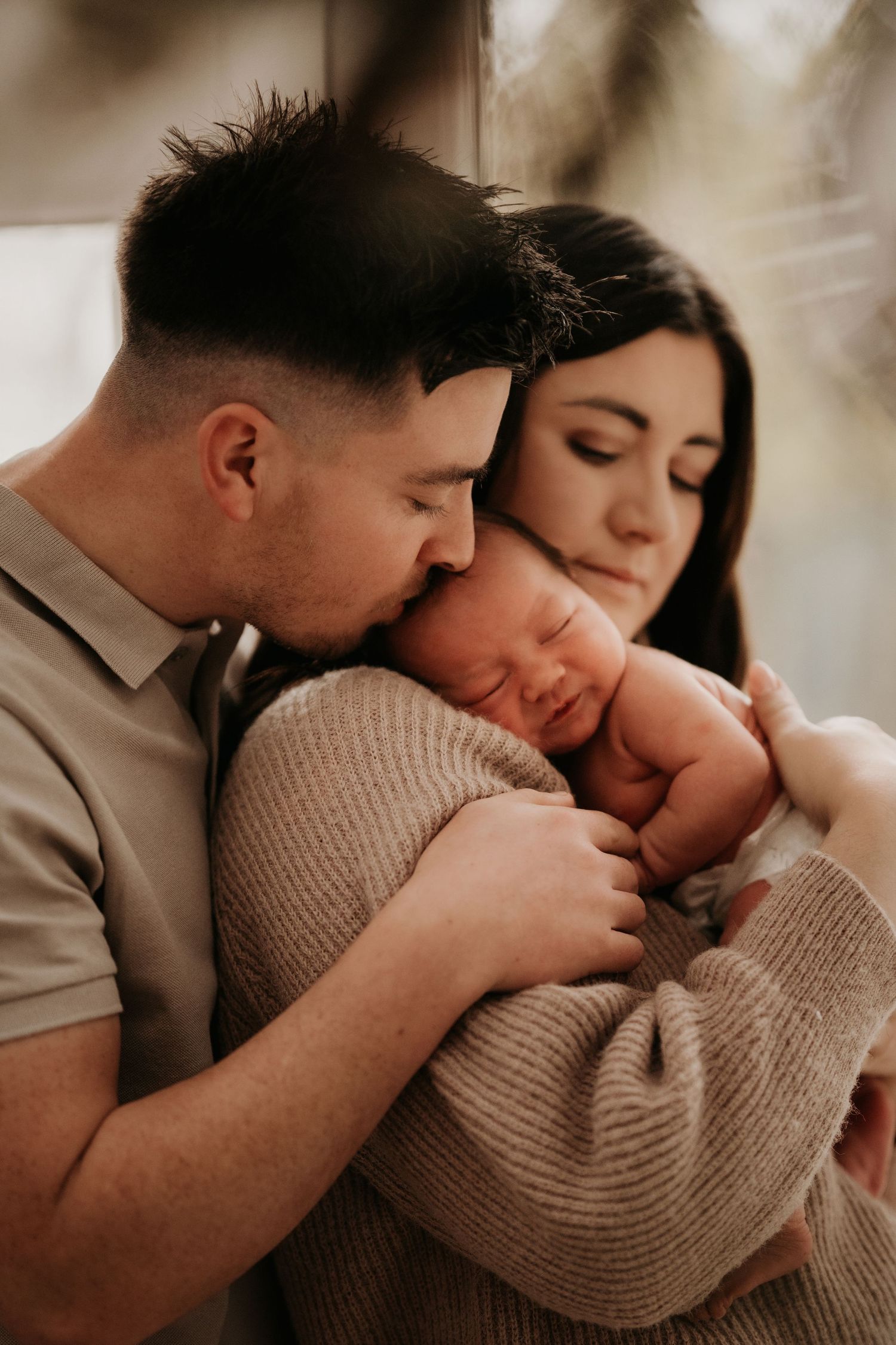 Parents holding their newborn close during a tender in-home family session in Hinckley