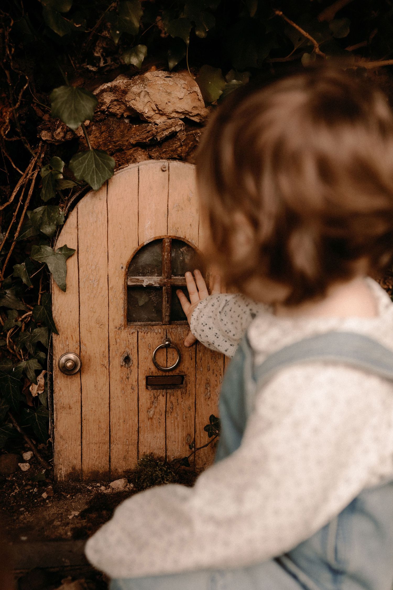 Child exploring a tiny garden door during a whimsical outdoor documentary childhood photography session.