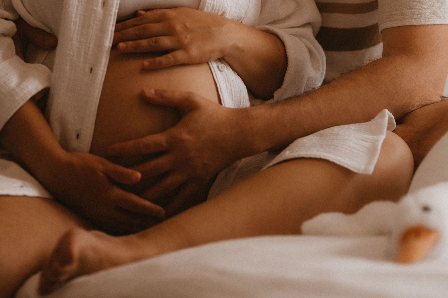 Hands holding a pregnant belly during an intimate maternity moment at home.