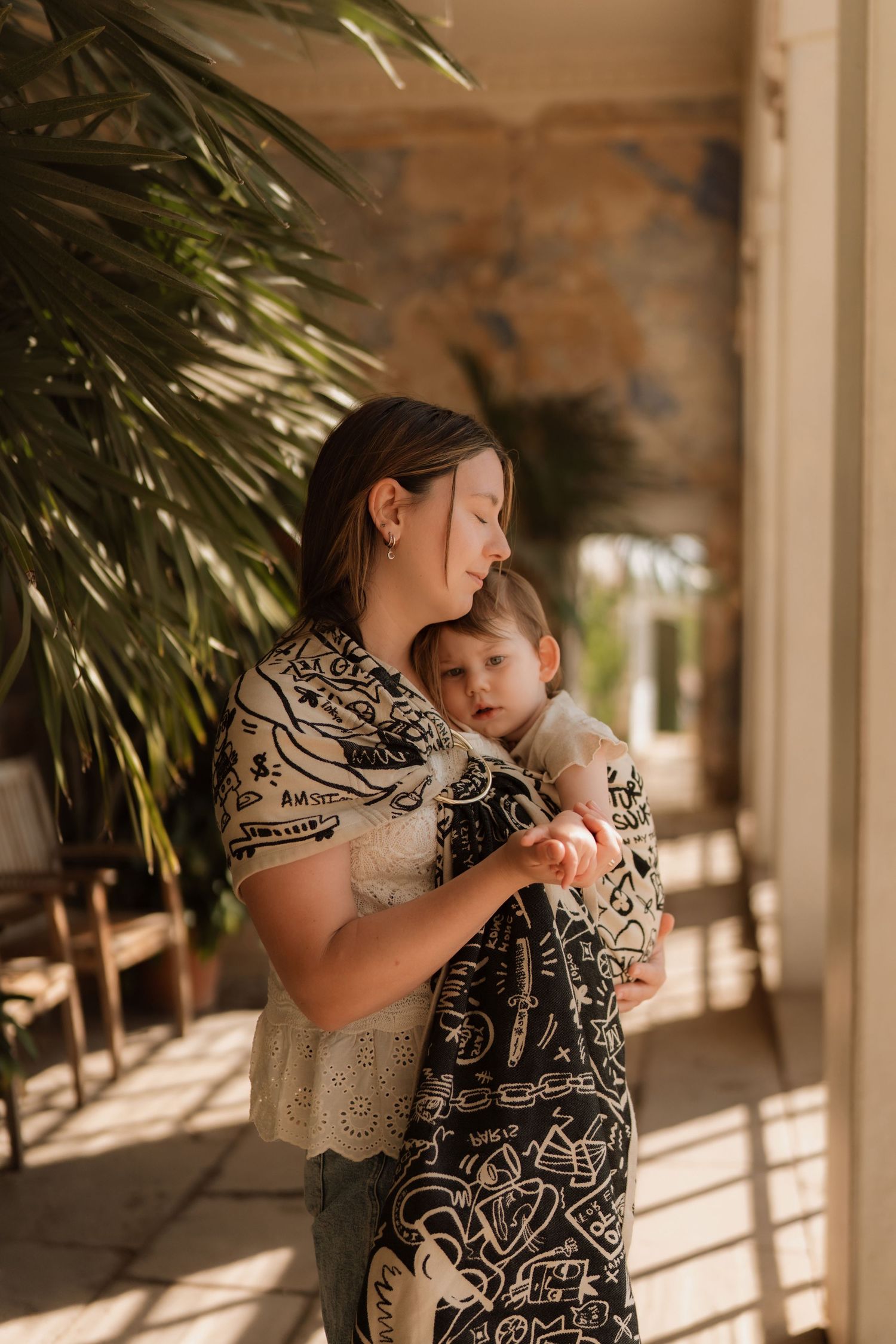 Mother holds her baby close while standing in warm sunlight during an emotional motherhood session.