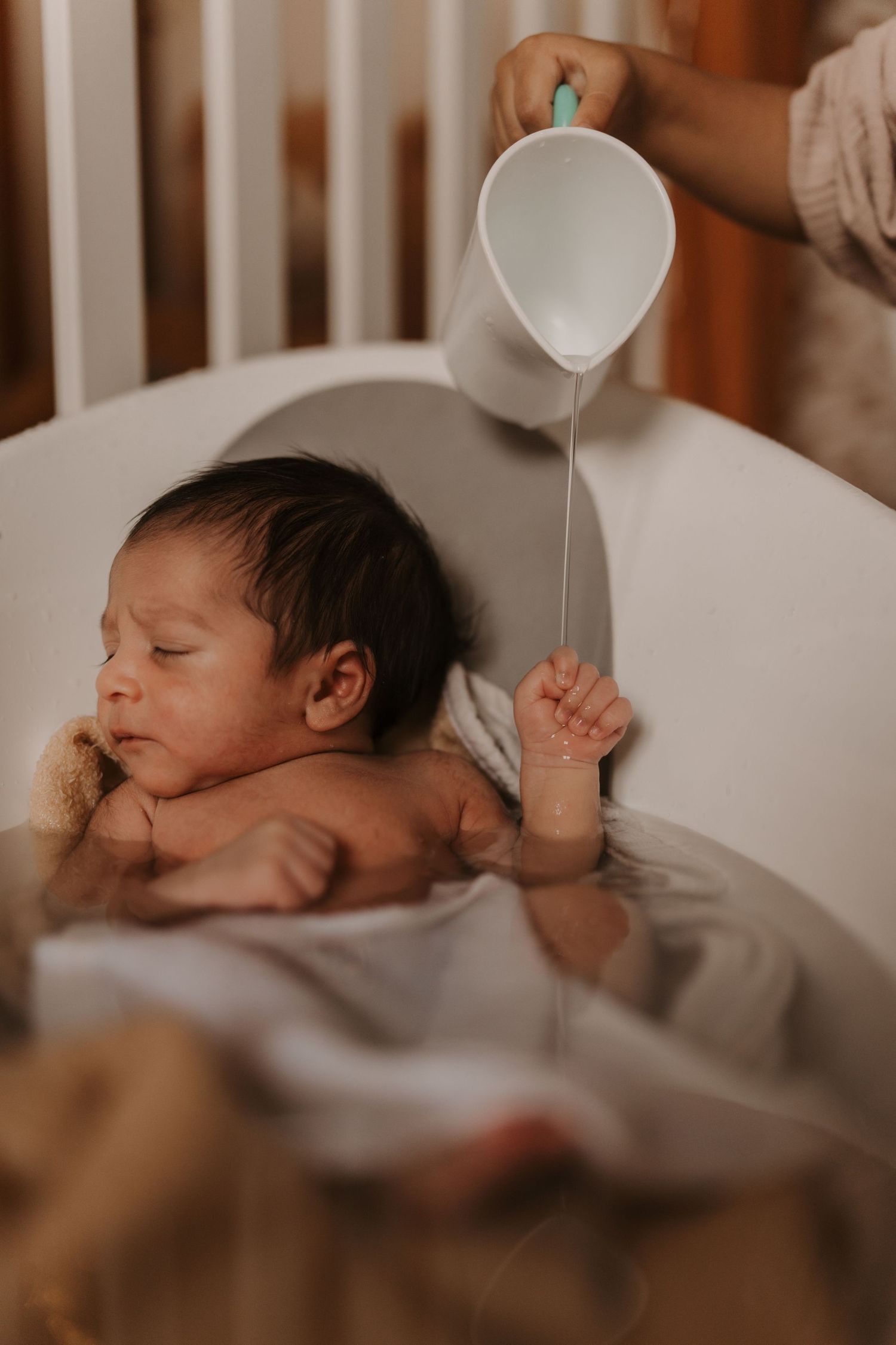 Parent pouring water over a newborn during a peaceful lifestyle newborn bath photoshoot at home.