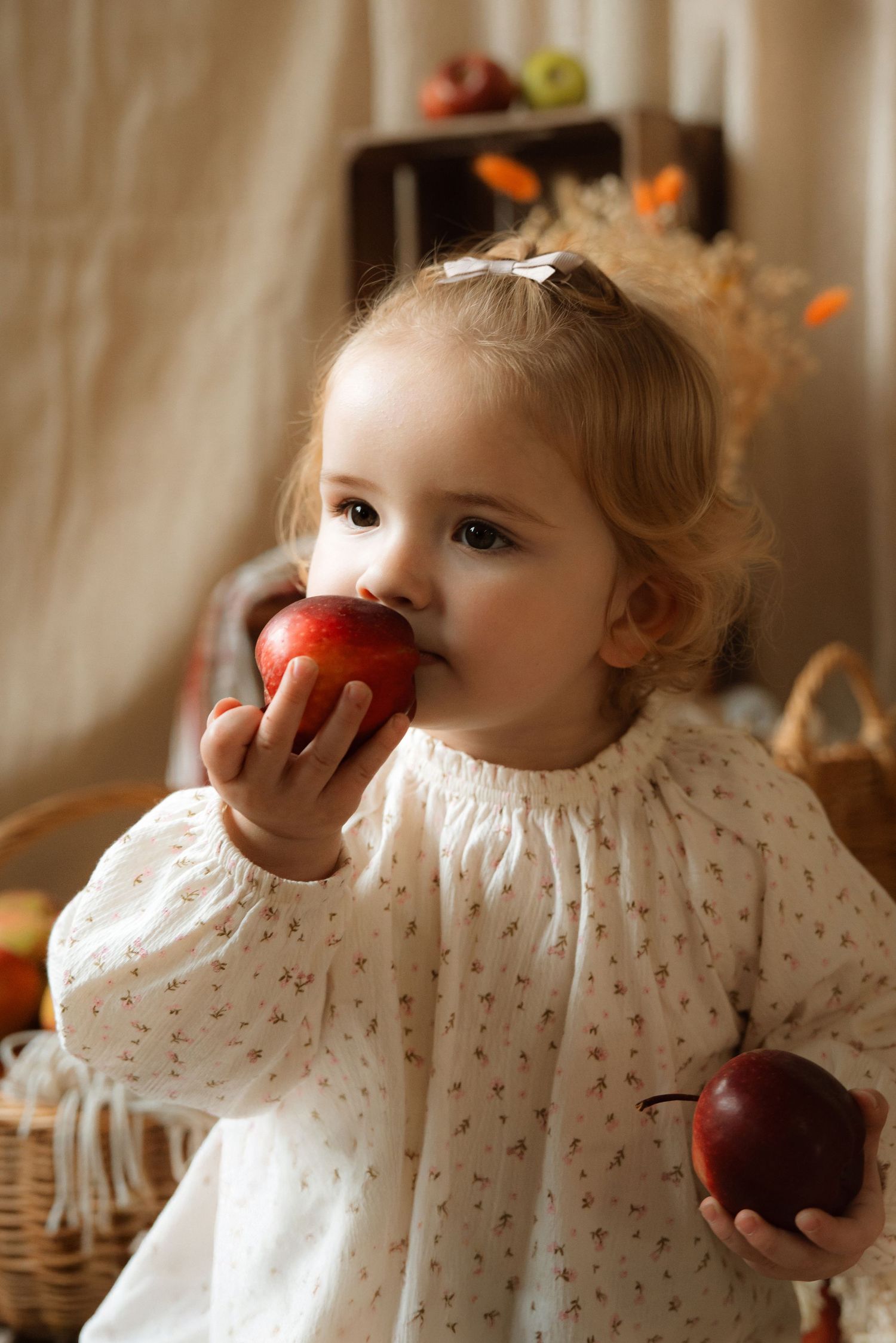 Toddler in cream dress eats an apple indoors during a natural lifestyle storytelling photoshoot. for Little Mess Burton