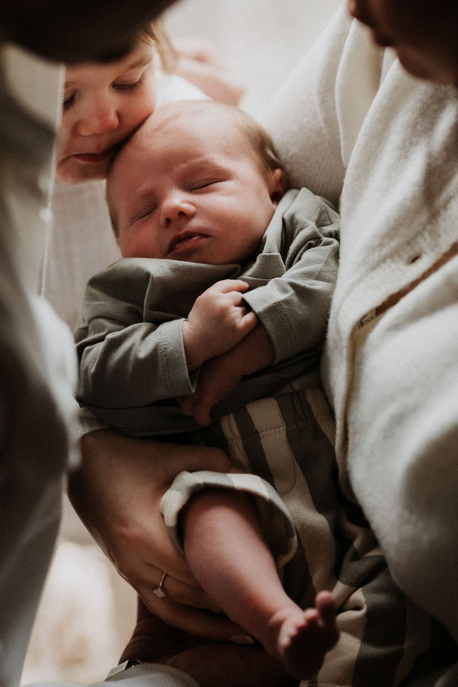 Newborn sleeping in a parent’s arms during a calm lifestyle newborn photoshoot at home in Ashby