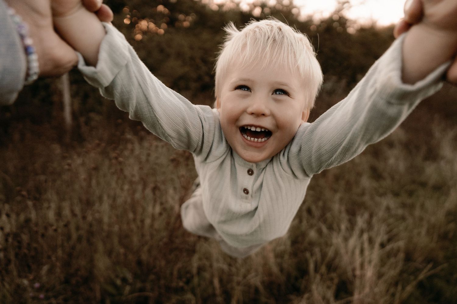 Child laughing while being lifted by their arms in a field