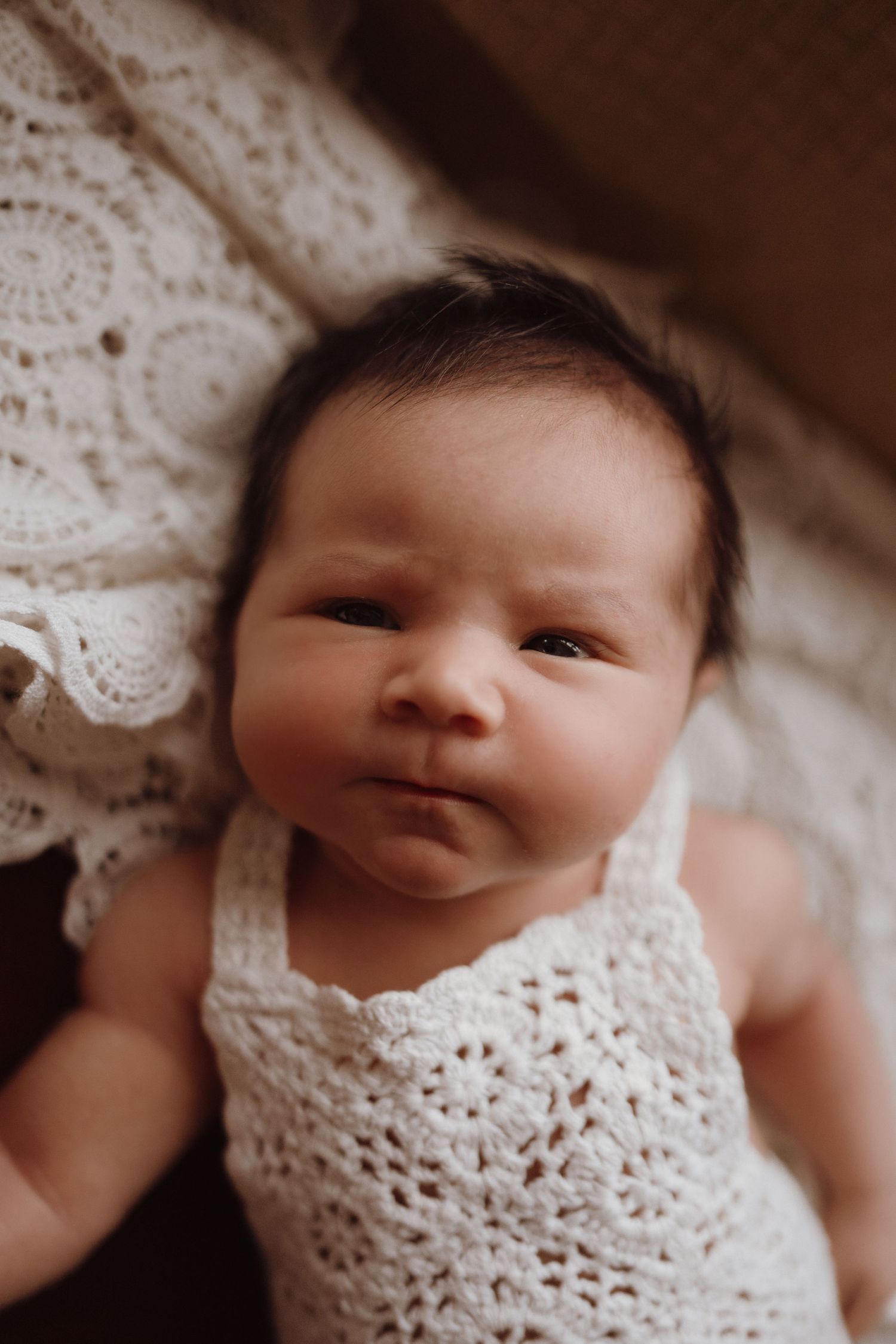 Newborn baby in a handmade crochet outfit lying on a soft blanket during a natural home session.