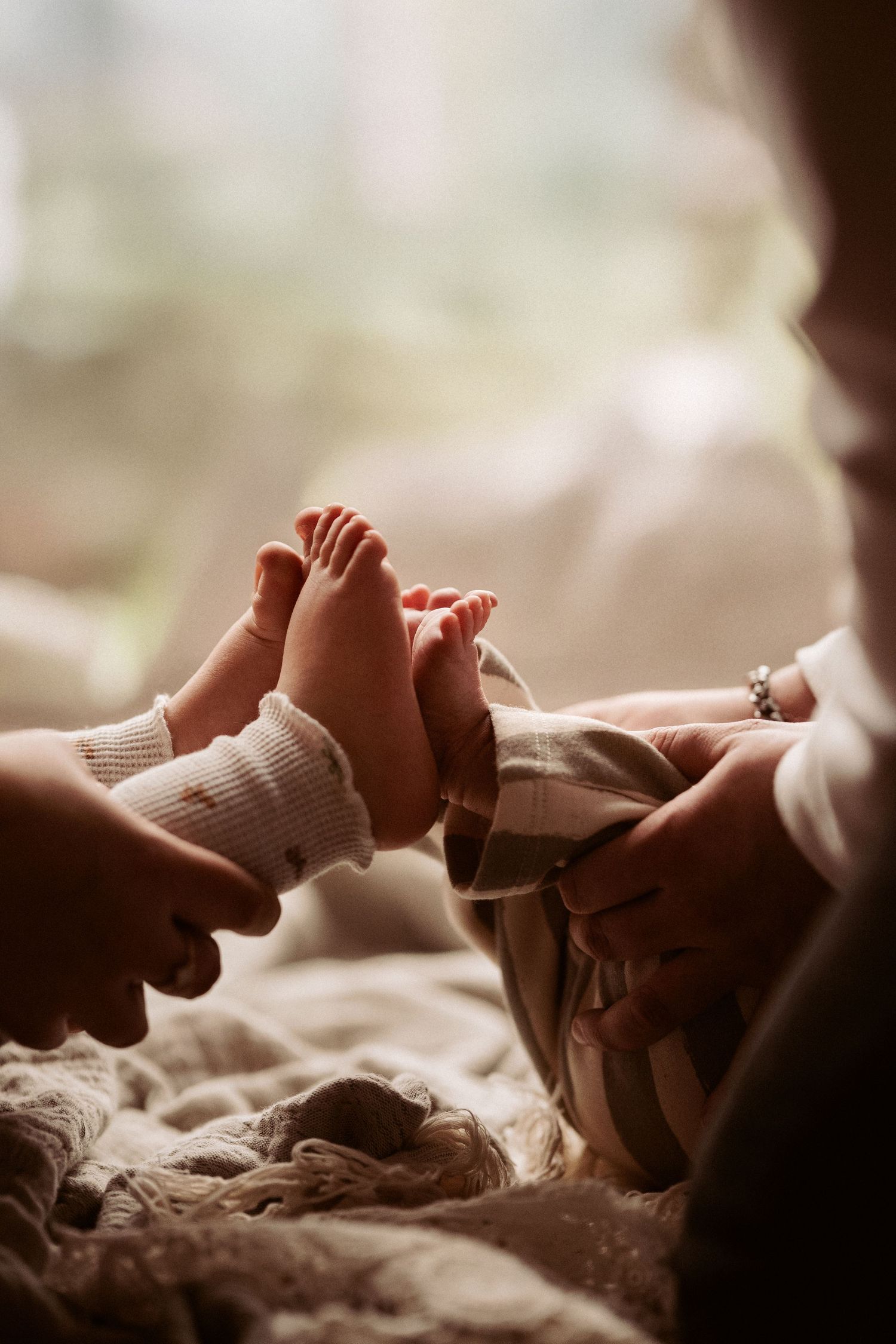 Tiny newborn feet held by parents in warm window light during an intimate storytelling photoshoot with soft stories by angela