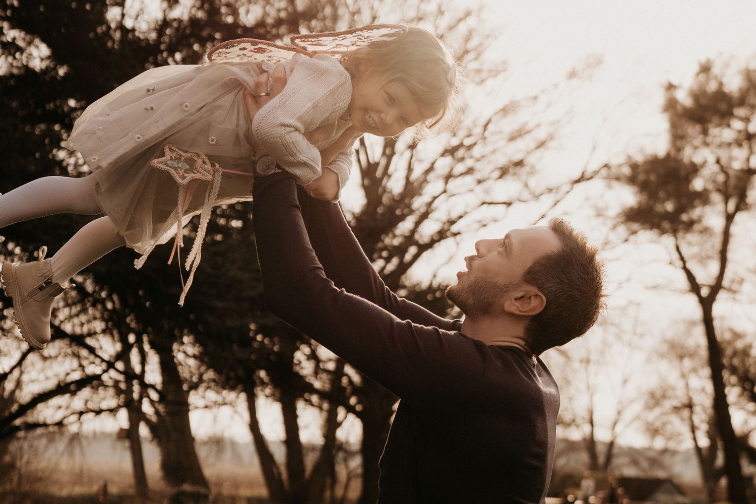 Father lifts his daughter in the air at sunset during a joyful outdoor family photoshoot in the Midlands, Lichfield