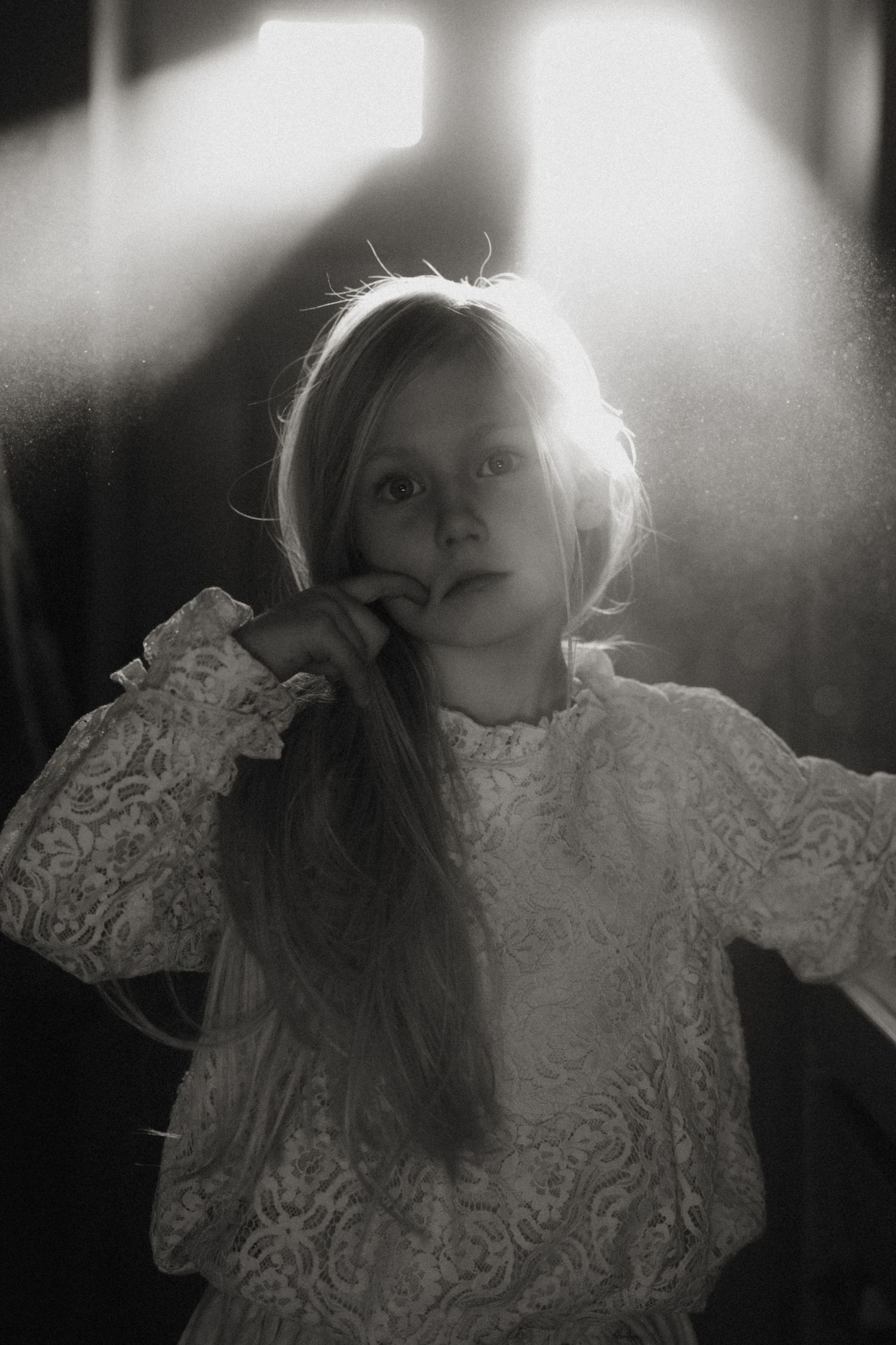 Child standing in soft window light during a black and white documentary childhood photoshoot in Swadlincote