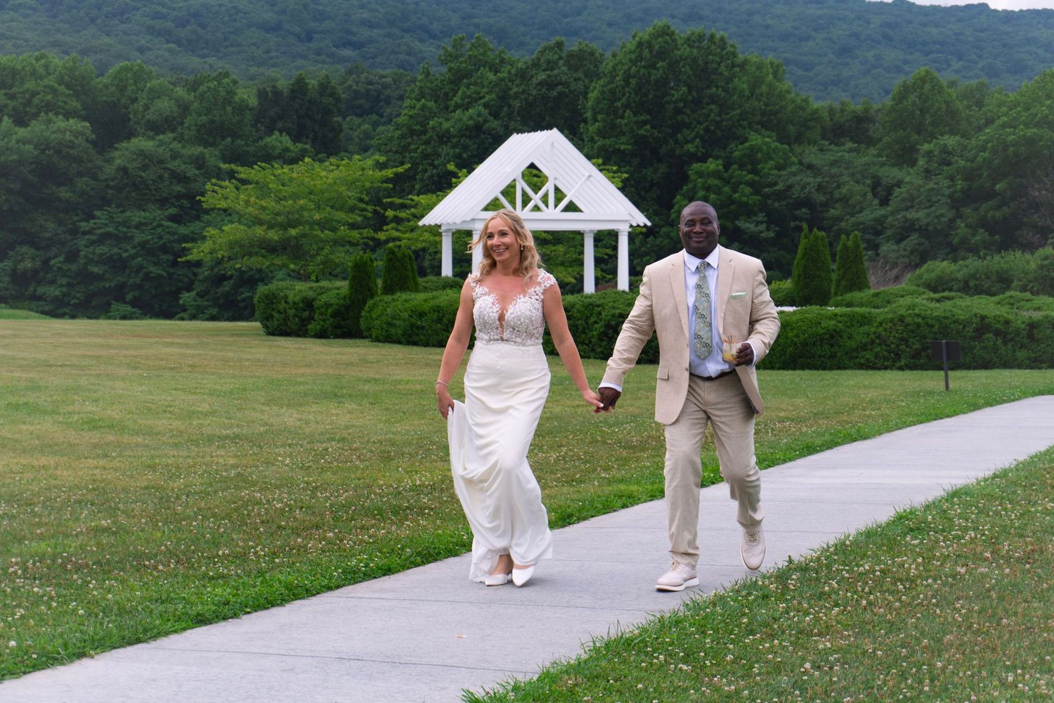 A newlywed couple holds hands as they walk into their wedding reception, greeted by guests.