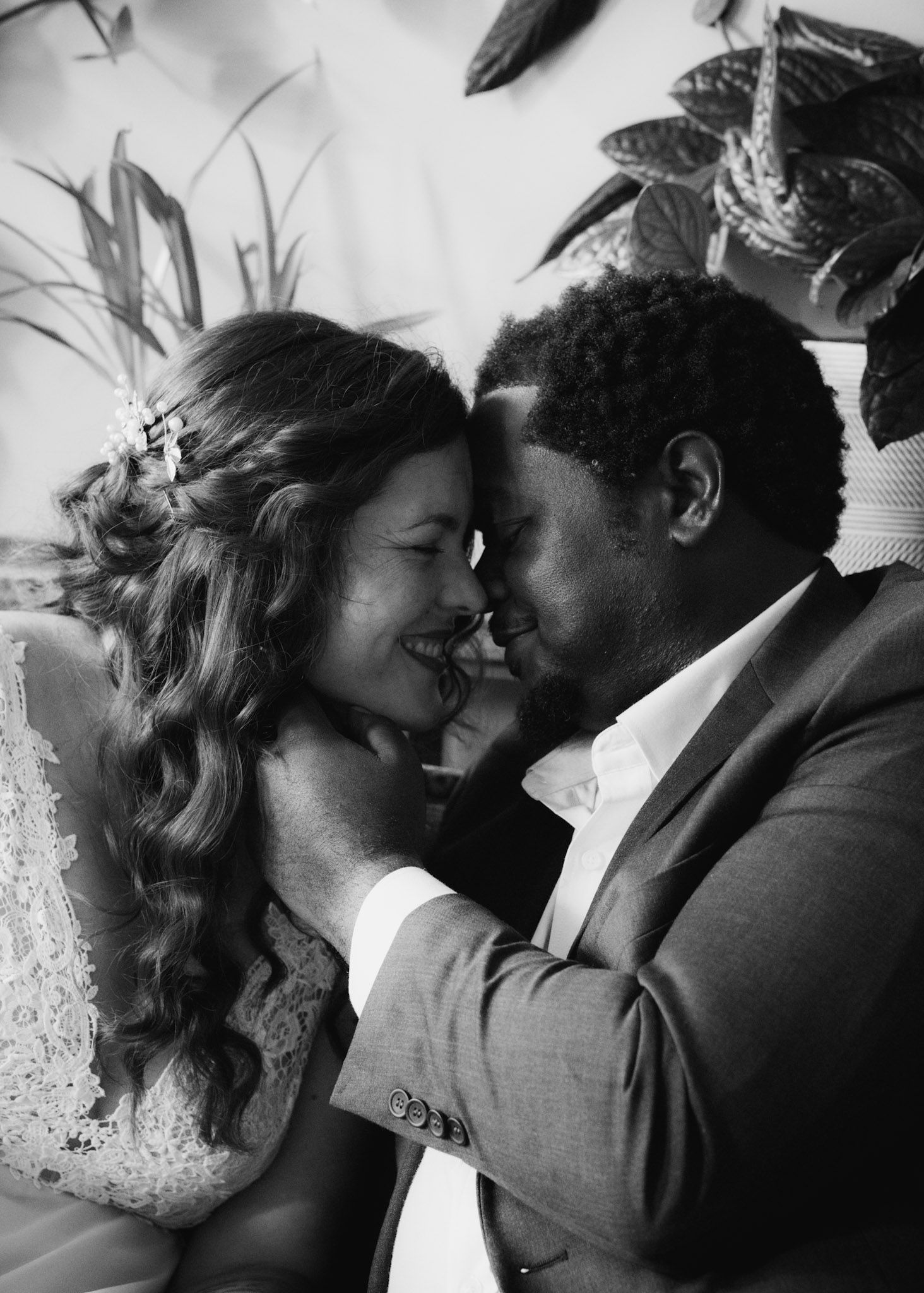 Black and white close-up portrait of a newlywed couple smiling as they lean in close, about to kiss.