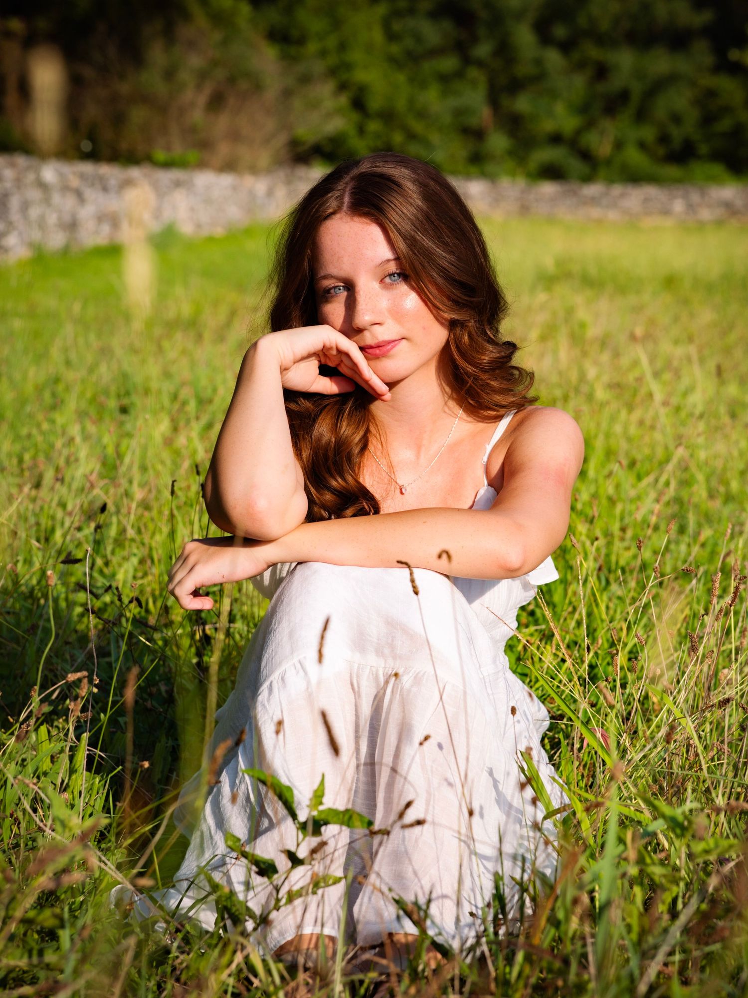 A color portrait of a young woman in a white dress smiling in a field of tall grass.