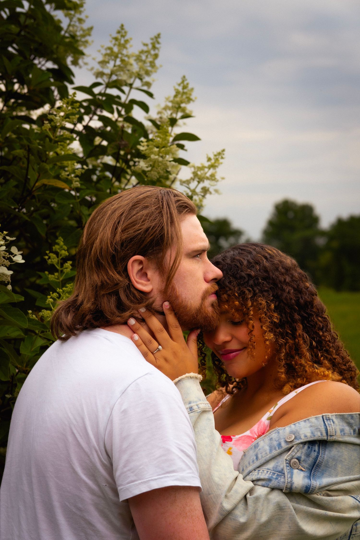 A tight close-up portrait of a couple with their faces pressed close together, one partner gently cradling the other's cheek.