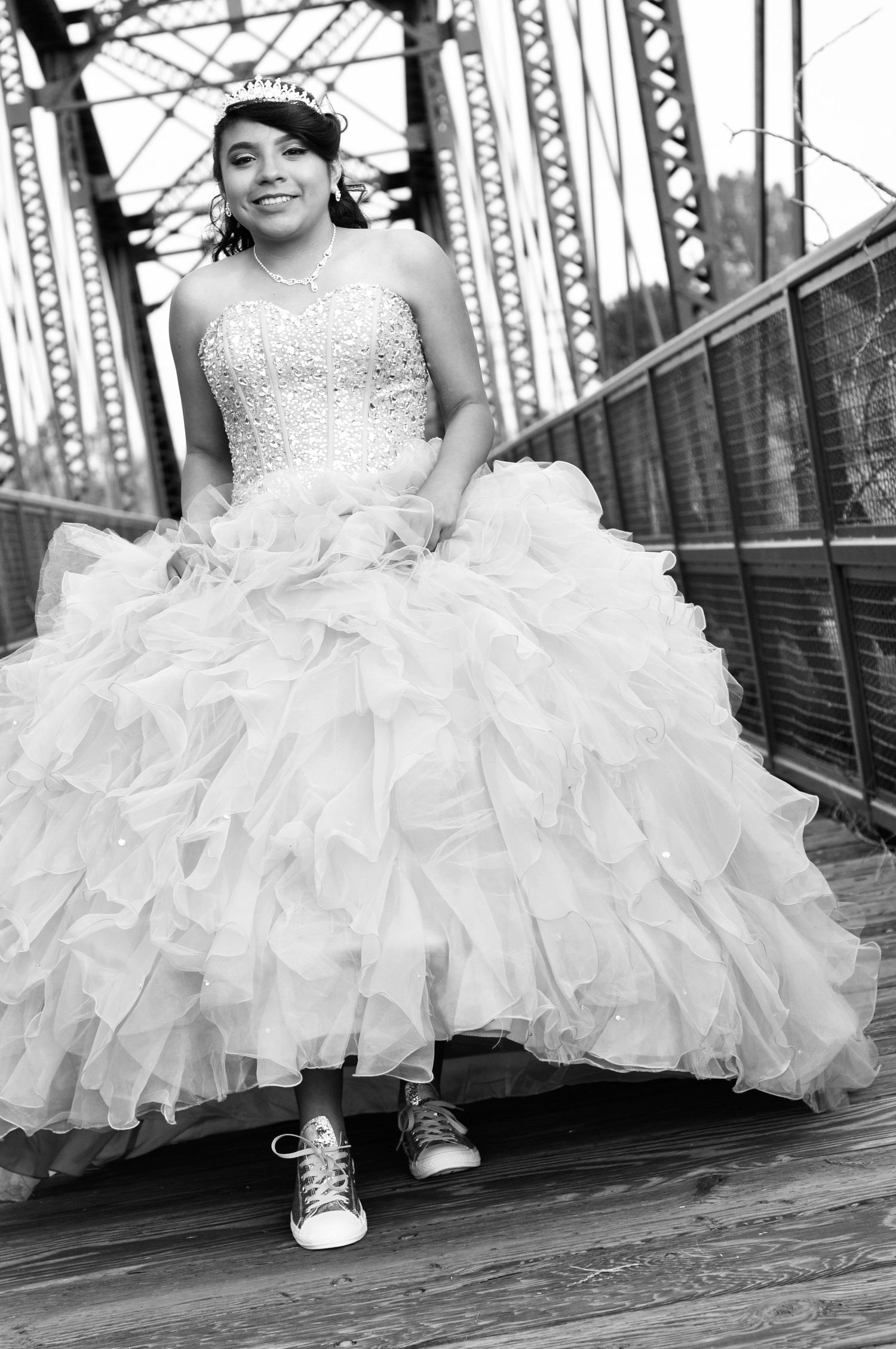 Quinceanera black and white portrait of teenage girl in formal dress with sneakers on a bridge