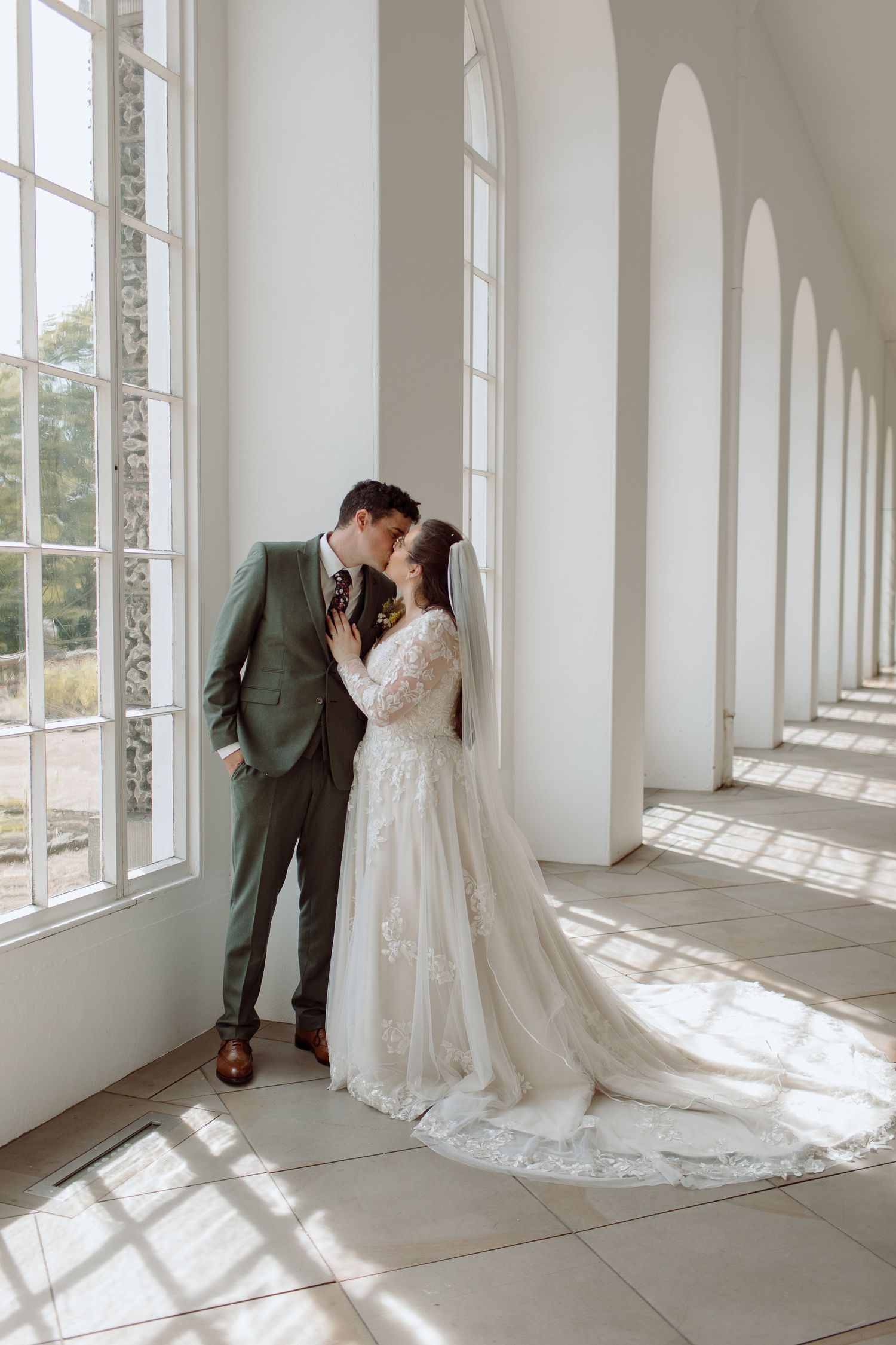 Bride and groom kissing under the grand arched windows at Margan Park Orangery in South Wales.