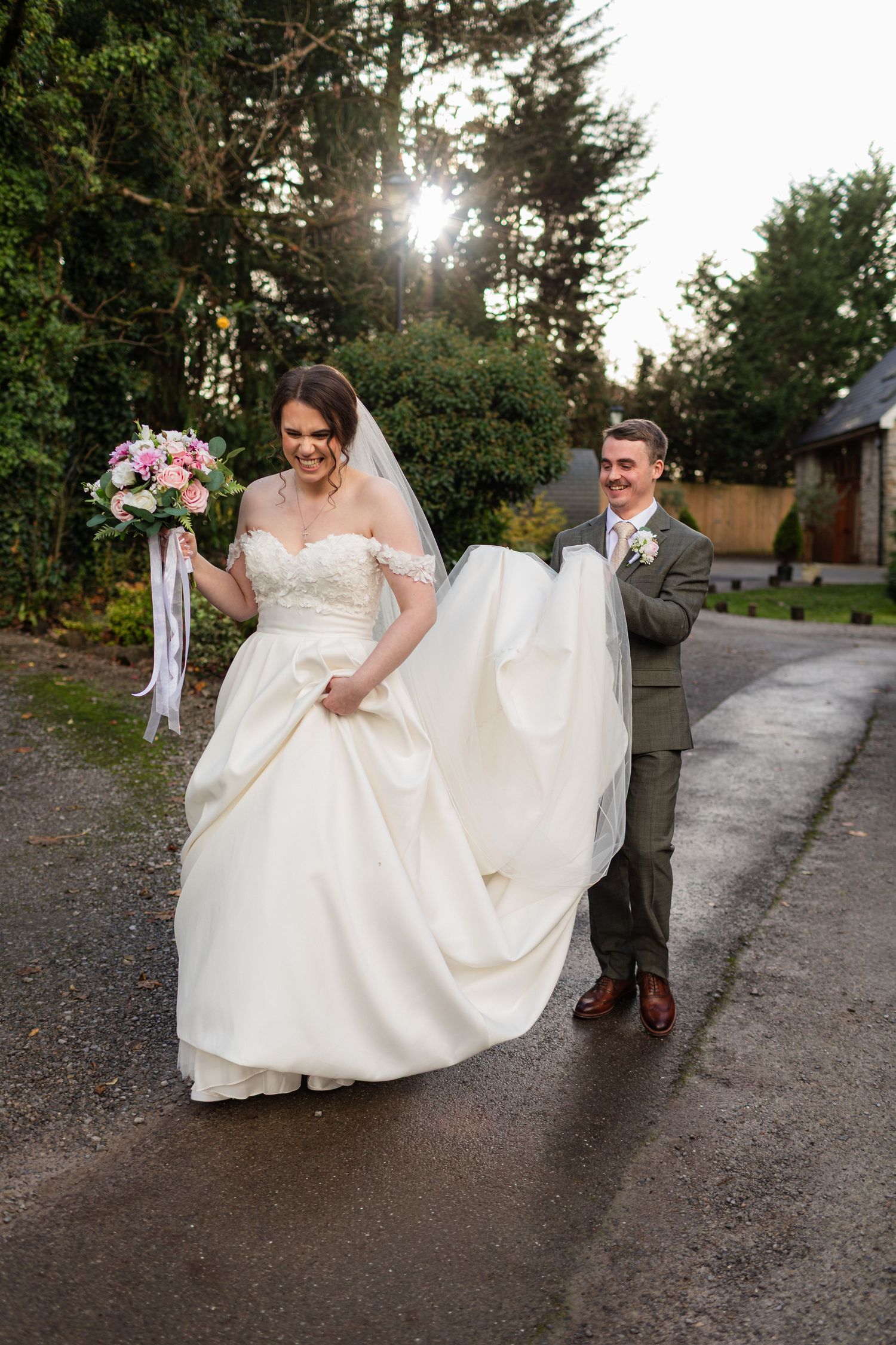Groom is helping his wife to carry her dress as they go for couple portraits on the grounds of Pencoed House Estate in Cardiff.
