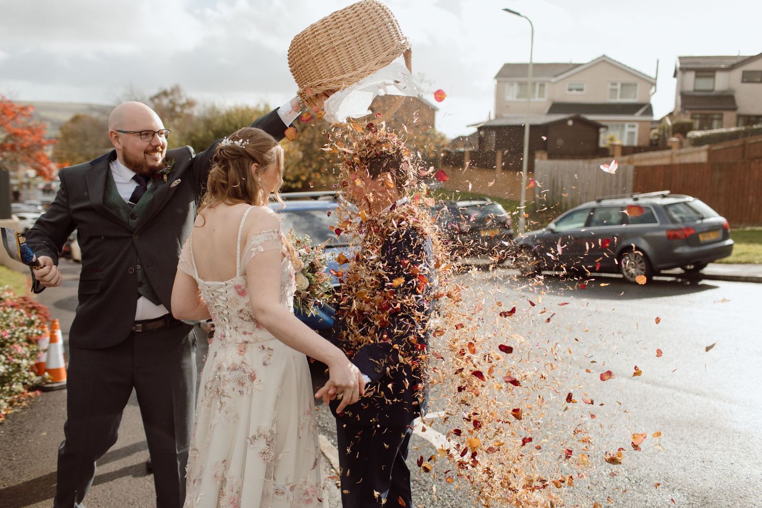 Bride & Groom stand on a path while the grooms brother throws and entire basket of confetti outside a church in Pontypridd.