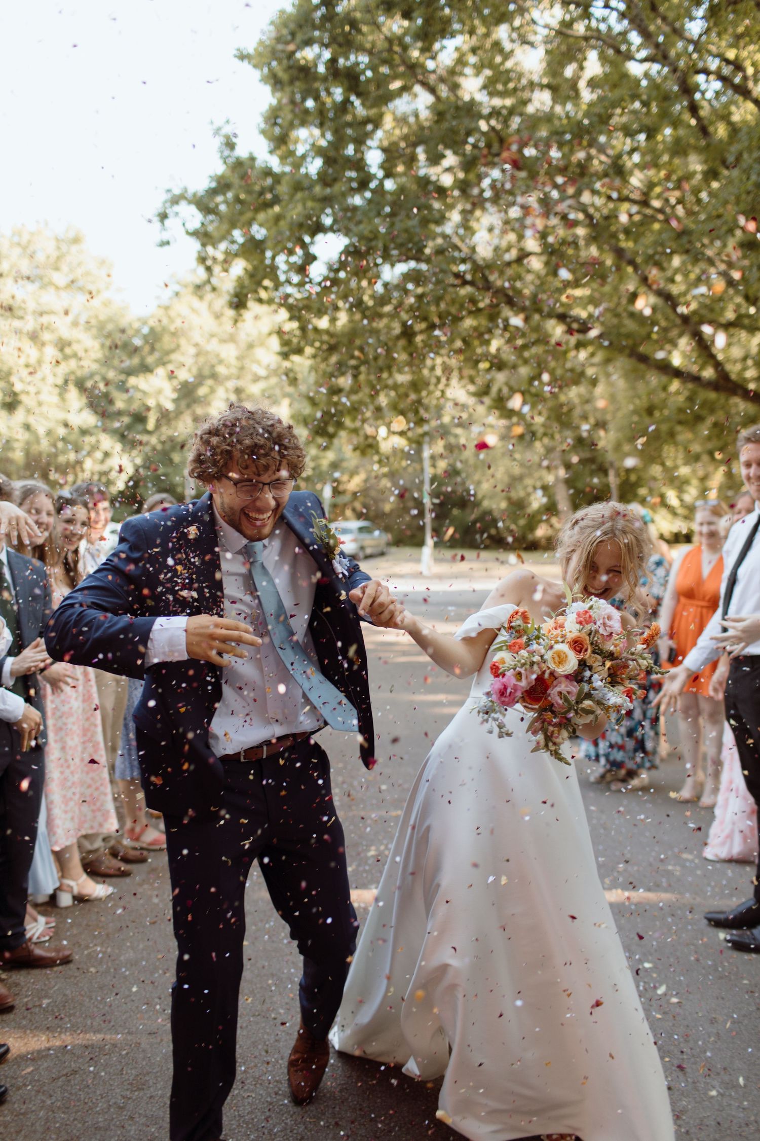 Bride and groom playfully ducking out of the way as their friend and family throw confetti at them in Heath Park, Cardiff.