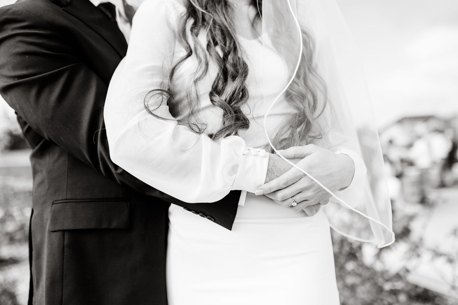 Black and white wedding photo showing couple embracing, with focus on bride's flowing dress and groom's dark suit.