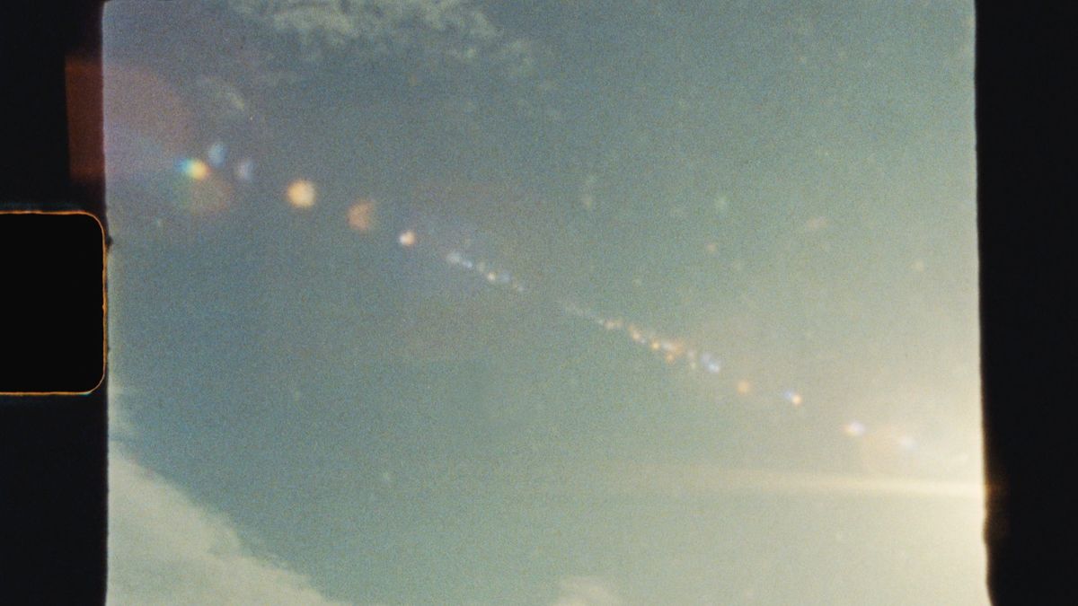 Multiple dots of sunlight create a lens flare pattern across a pale blue sky.