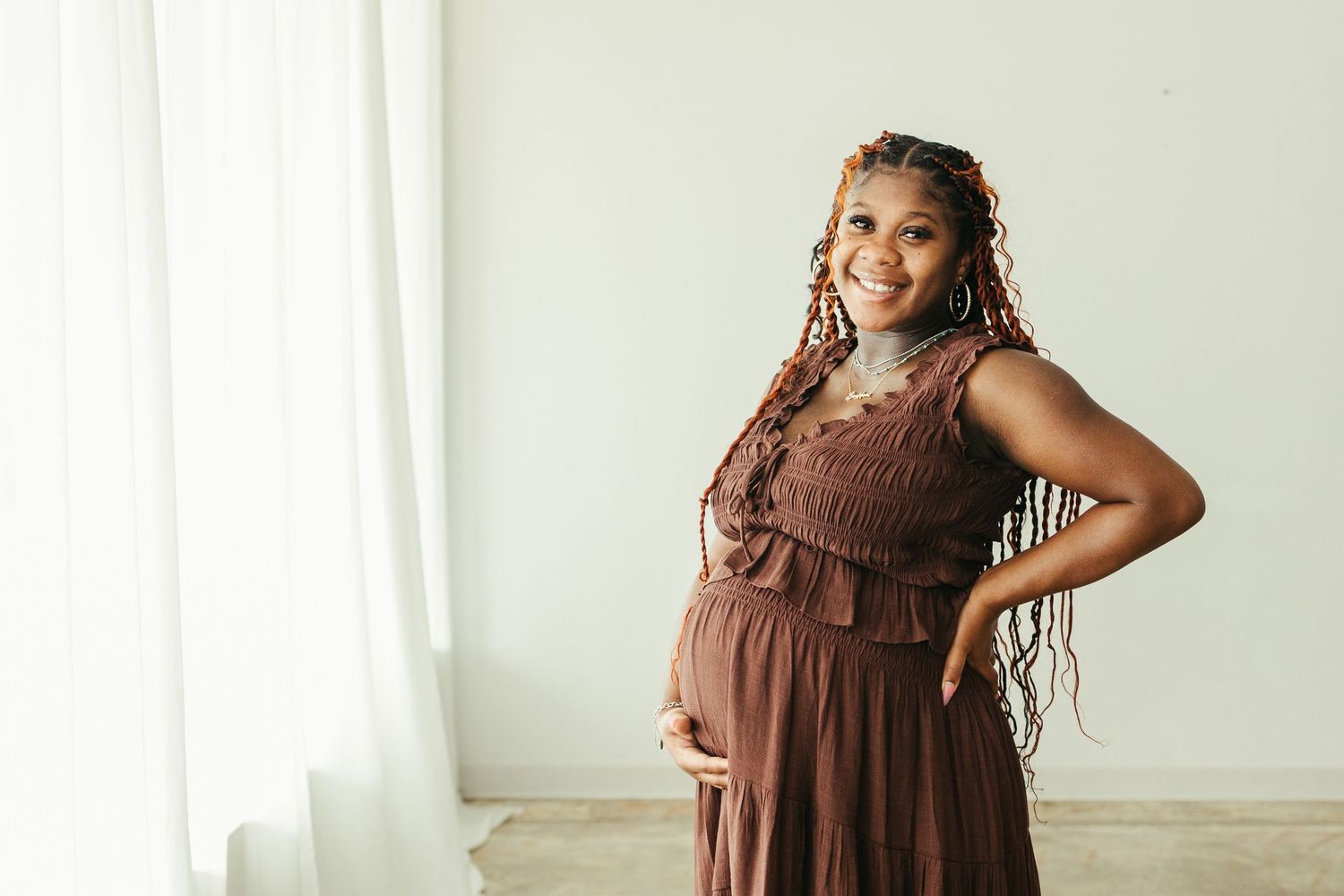 Smiling pregnant Black woman in brown ruffled maxi dress posing with hand on hip in Pearland maternity photos