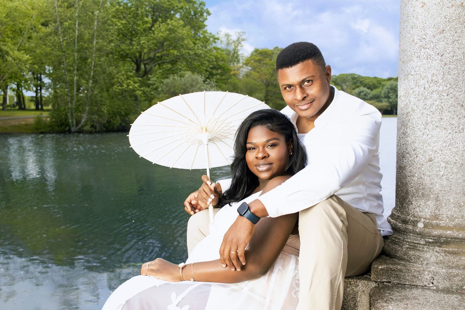Romantic outdoor couple photoshoot near lake with white pillars and natural scenery.