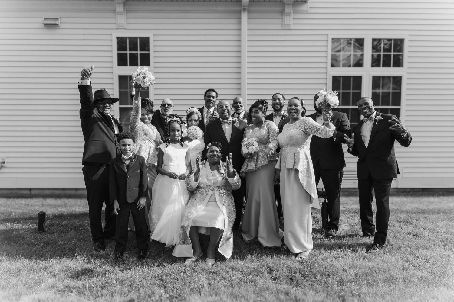Black and white panoramic photo of wedding party members lined up outside a traditional white building.