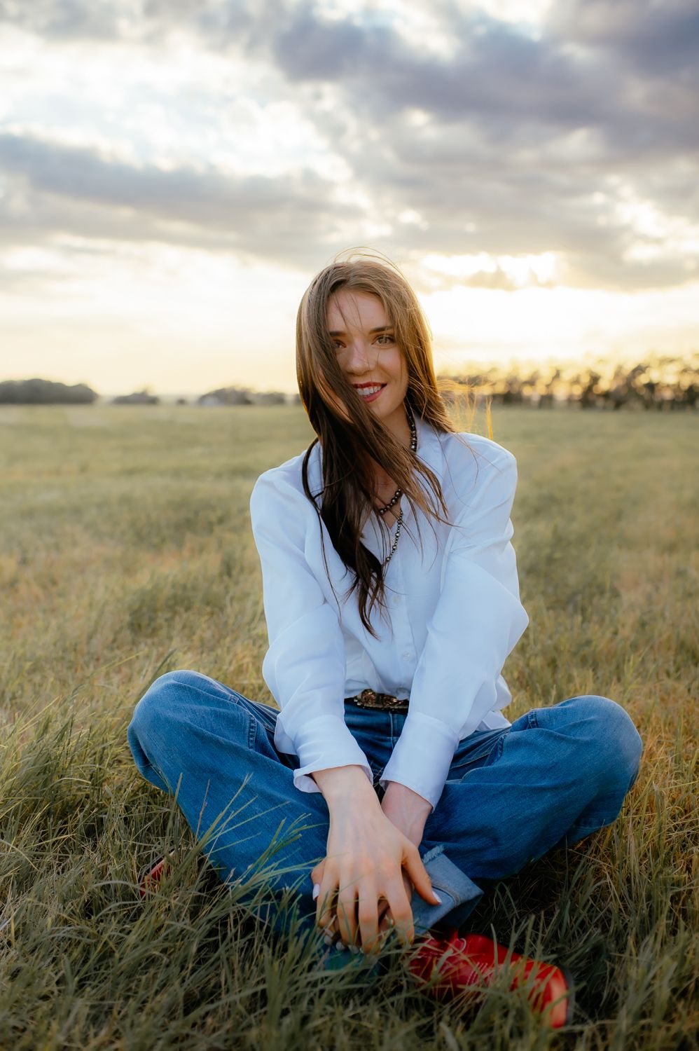 Oklahoma girl sitting cross legged and hair blowing in the wind, during Enid senior photos.