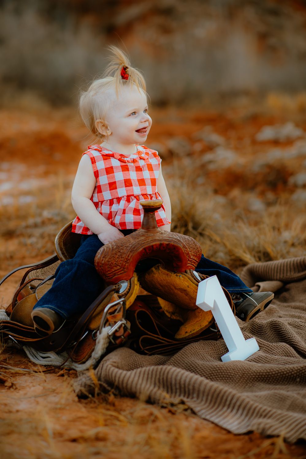 A little girl siting on a saddle for her one-year milestone photos with a family photographer at the Gloss Mountain, near Enid Oklahoma.