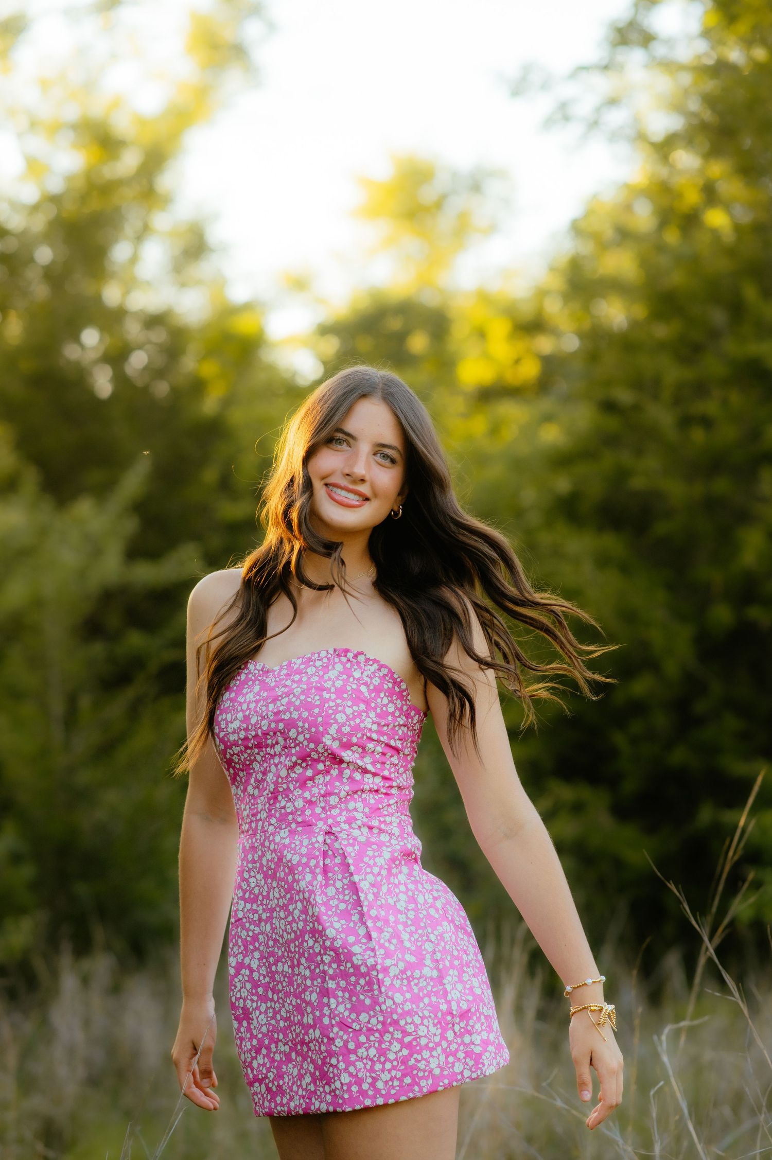 Senior girl in a floral dress laughing in tall grass during golden hour for Enid senior photos.