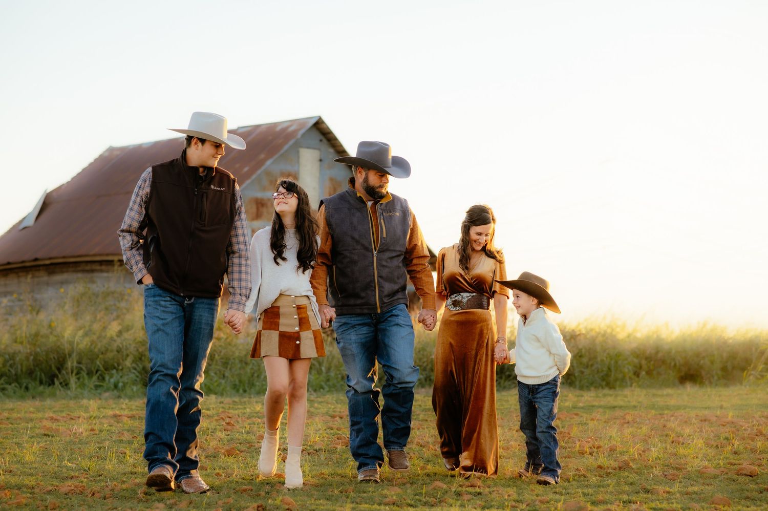 Family holding hands and walking in a field for western themed family photos with Enid OK photographer.