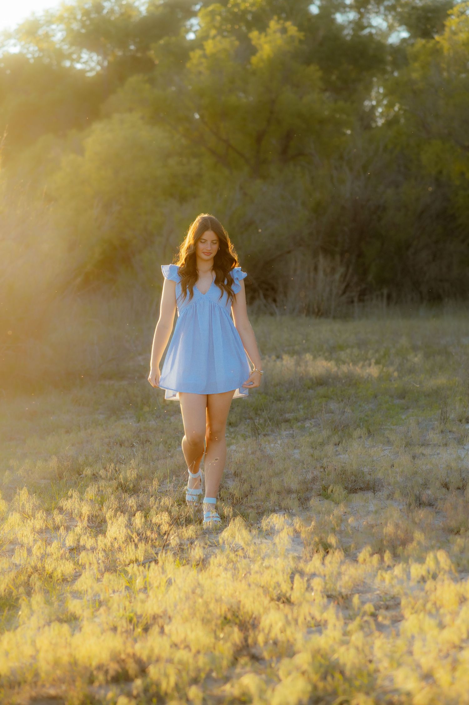 Girl in blue dress walking during golden hour captured by Enid senior photographer.
