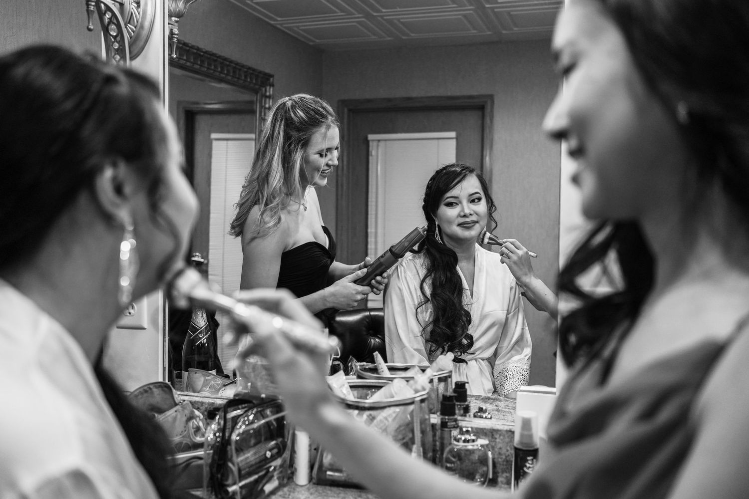 Bridesmaids helping bride with hair and makeup in black and white photo.
