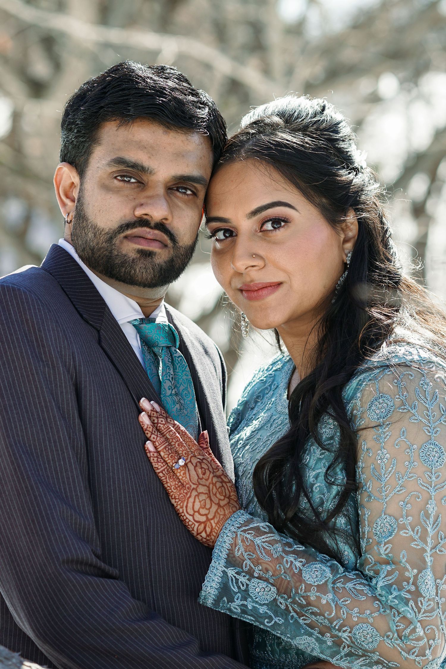 Close-up portrait of South Asian bride and groom with henna hands against a winter backdrop.