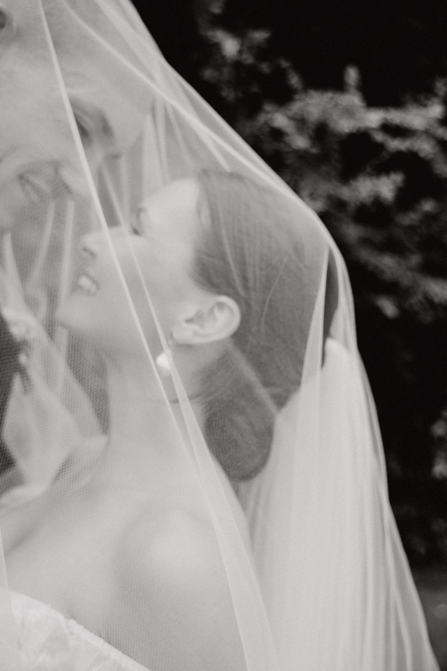 Romantic wedding couple sharing an intimate moment under a flowing white veil.