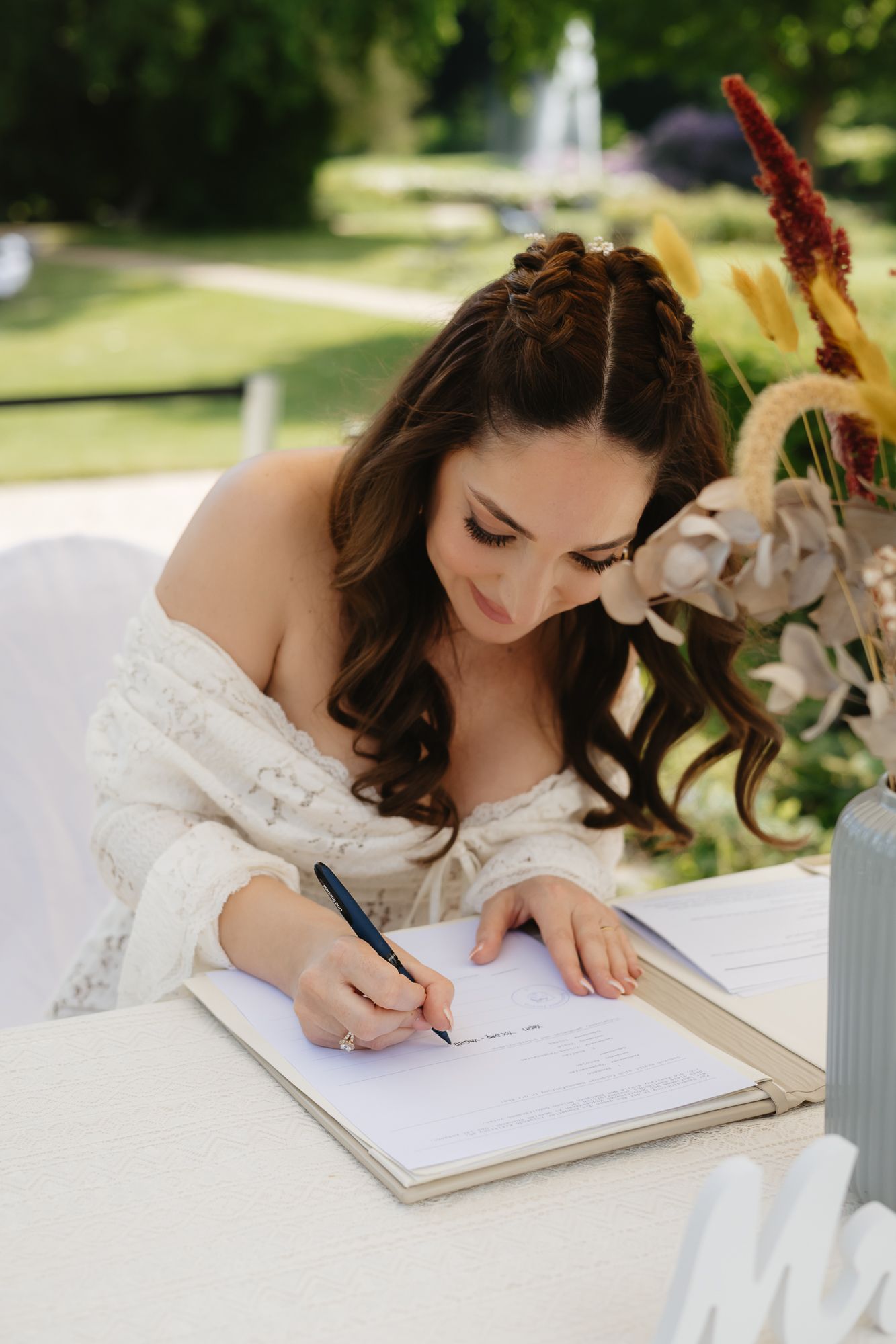 A close-up shot of someone signing a wedding document with a decorative pen on a white surface.