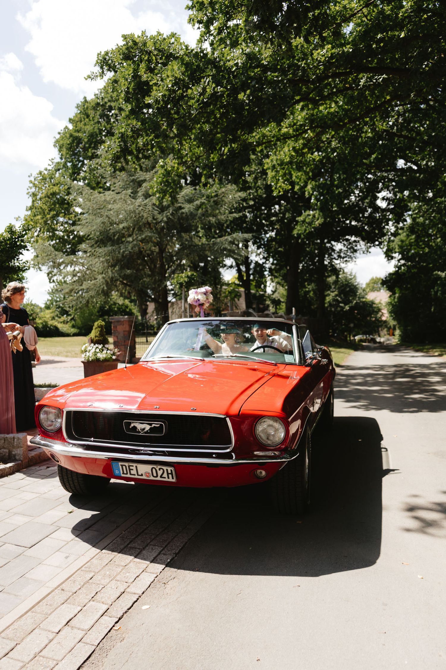 A classic red Ford Mustang convertible parked on a sunny day with trees in the background.
