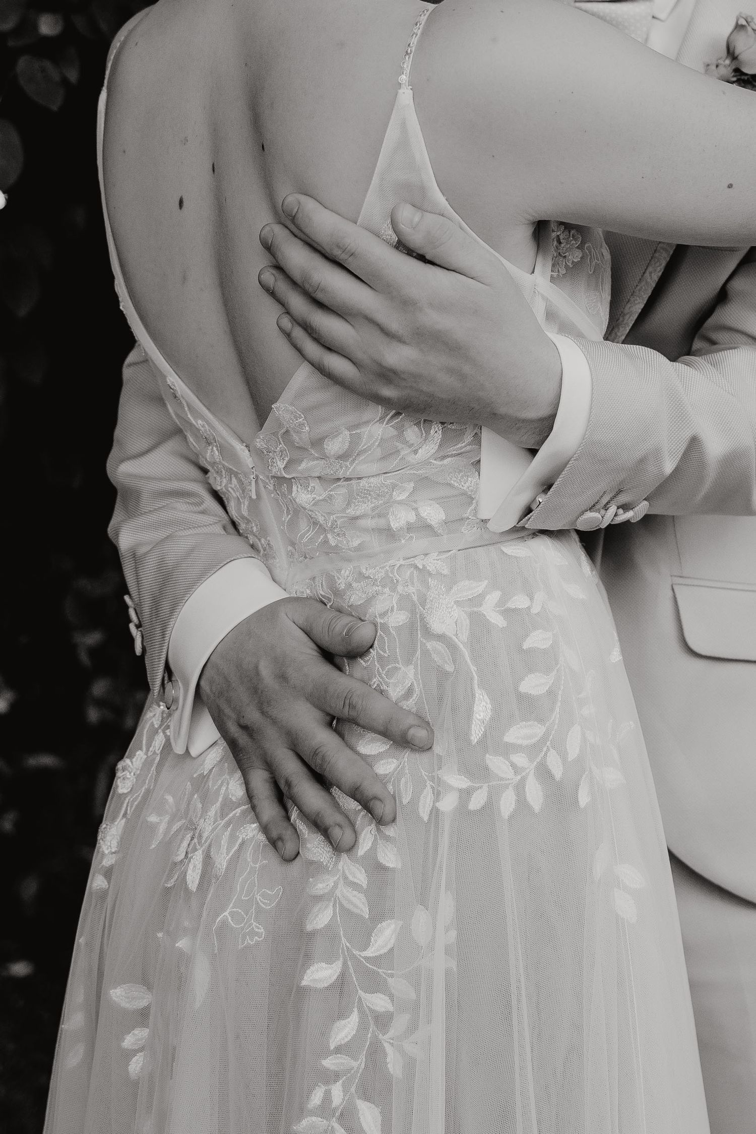 A series of black and white wedding photos showing close-up details of hands embracing around a delicate lace wedding dress.