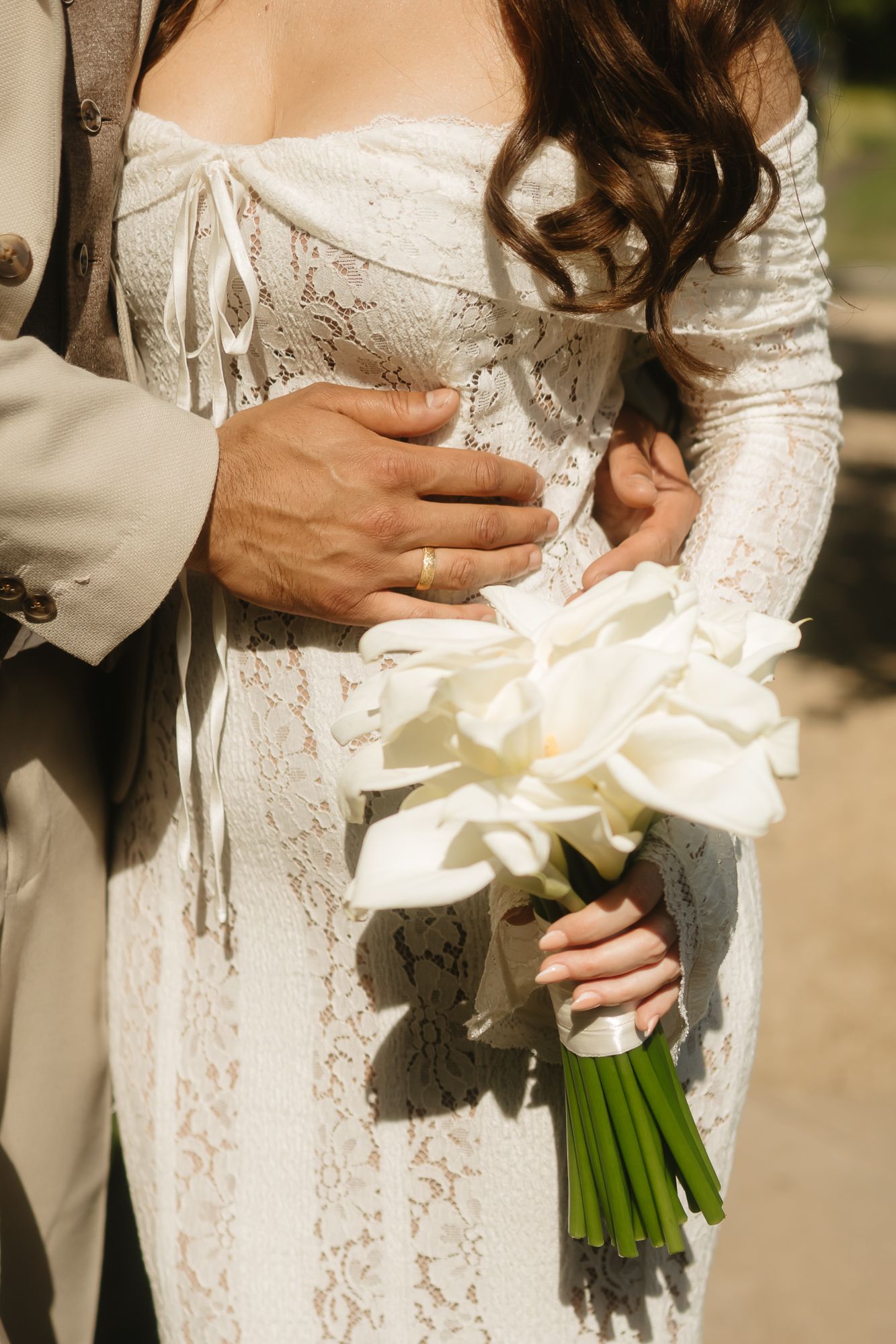 Detail shots of white wedding bouquet held against lace dress.