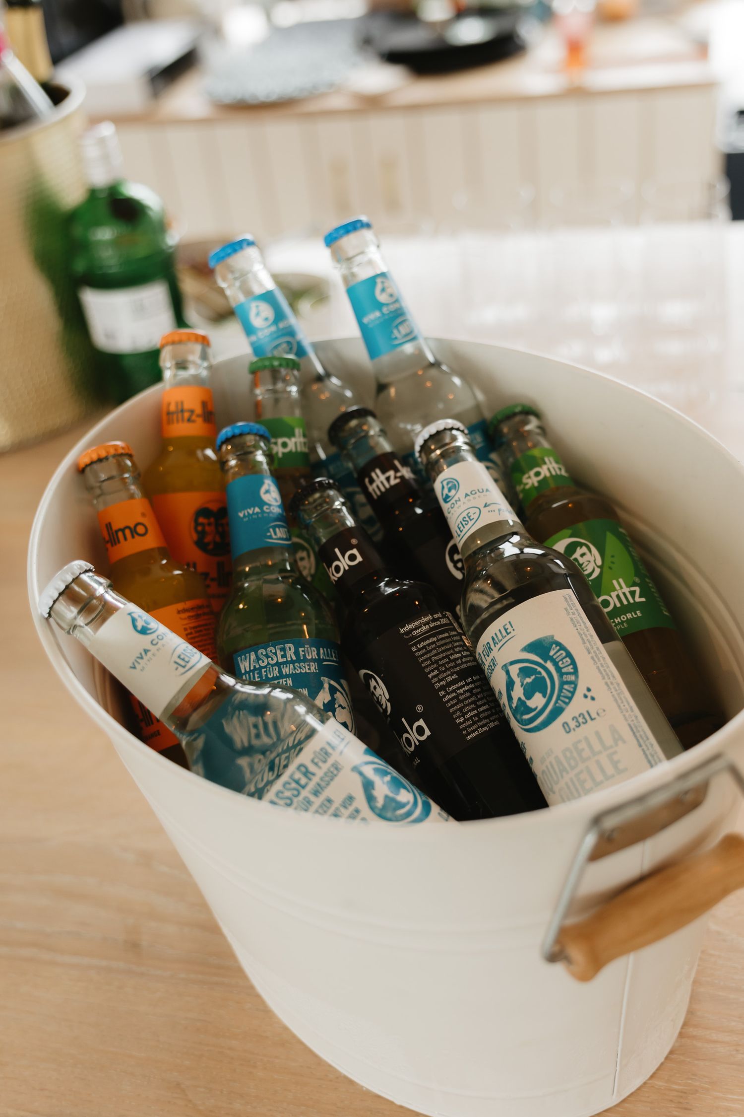 Various bottles of alcoholic beverages chilling in a white ice bucket on a wooden surface.