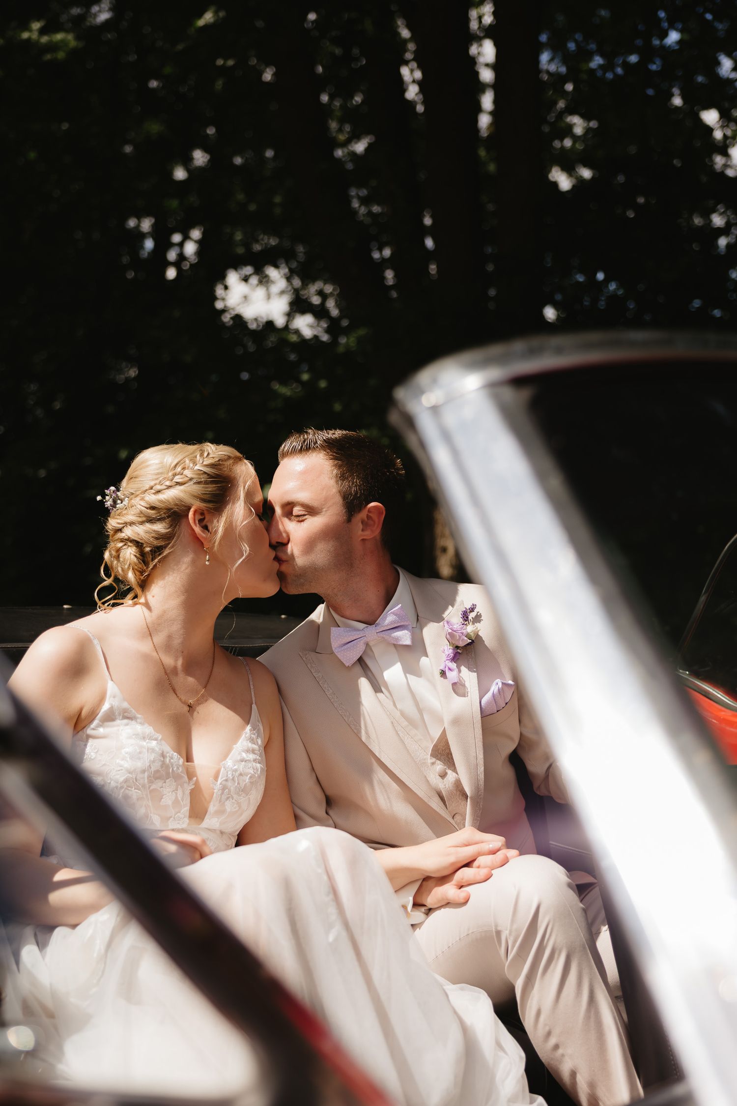 A romantic wedding couple shares a tender kiss while seated together outdoors in natural lighting.