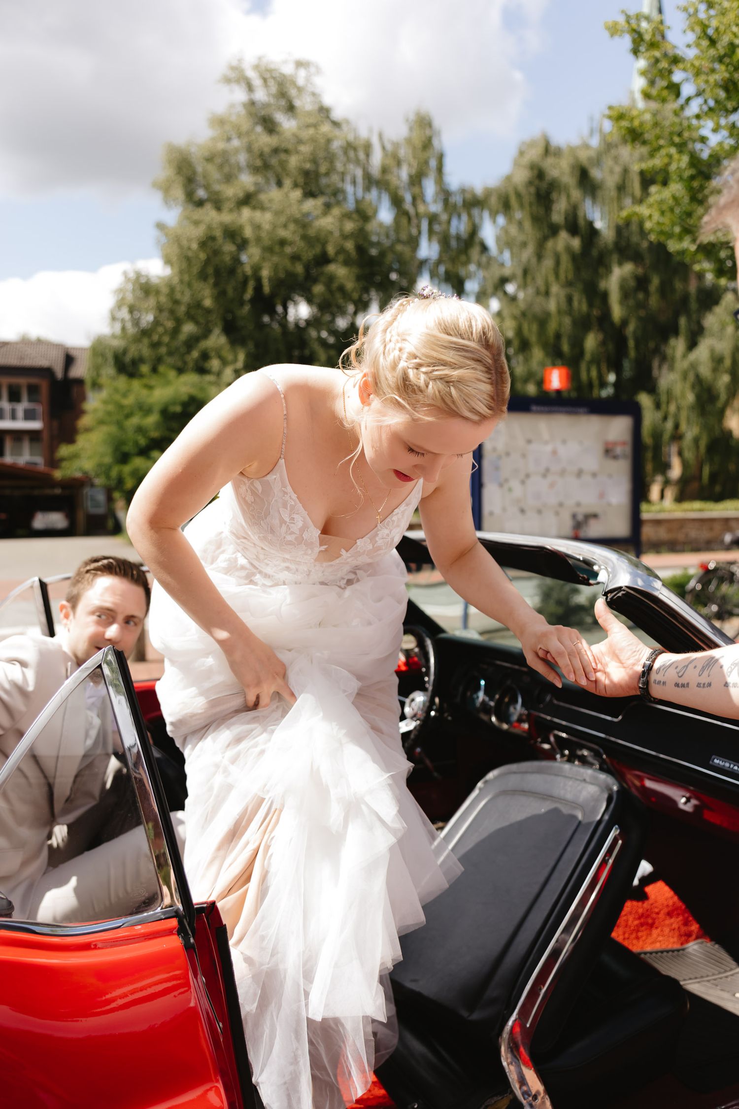Sequence of a bride in white dress gracefully entering a classic red and black vintage car on her wedding day.