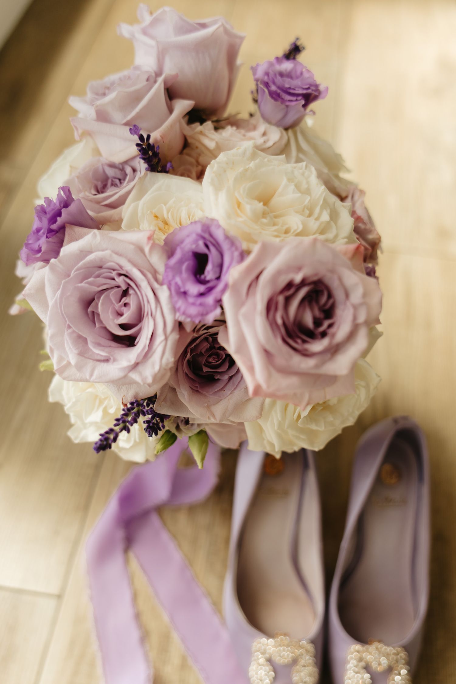 Elegant wedding bouquet with purple and cream roses displayed next to beige bridal shoes with crystal embellishments.