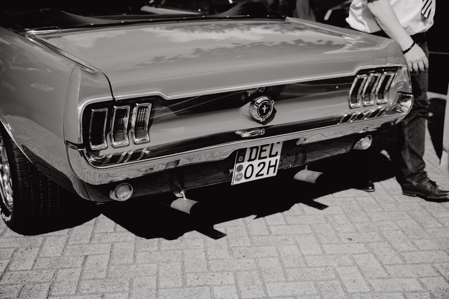 Classic Ford Mustang rear view details showing iconic triple taillights and chrome bumper in black and white photography.