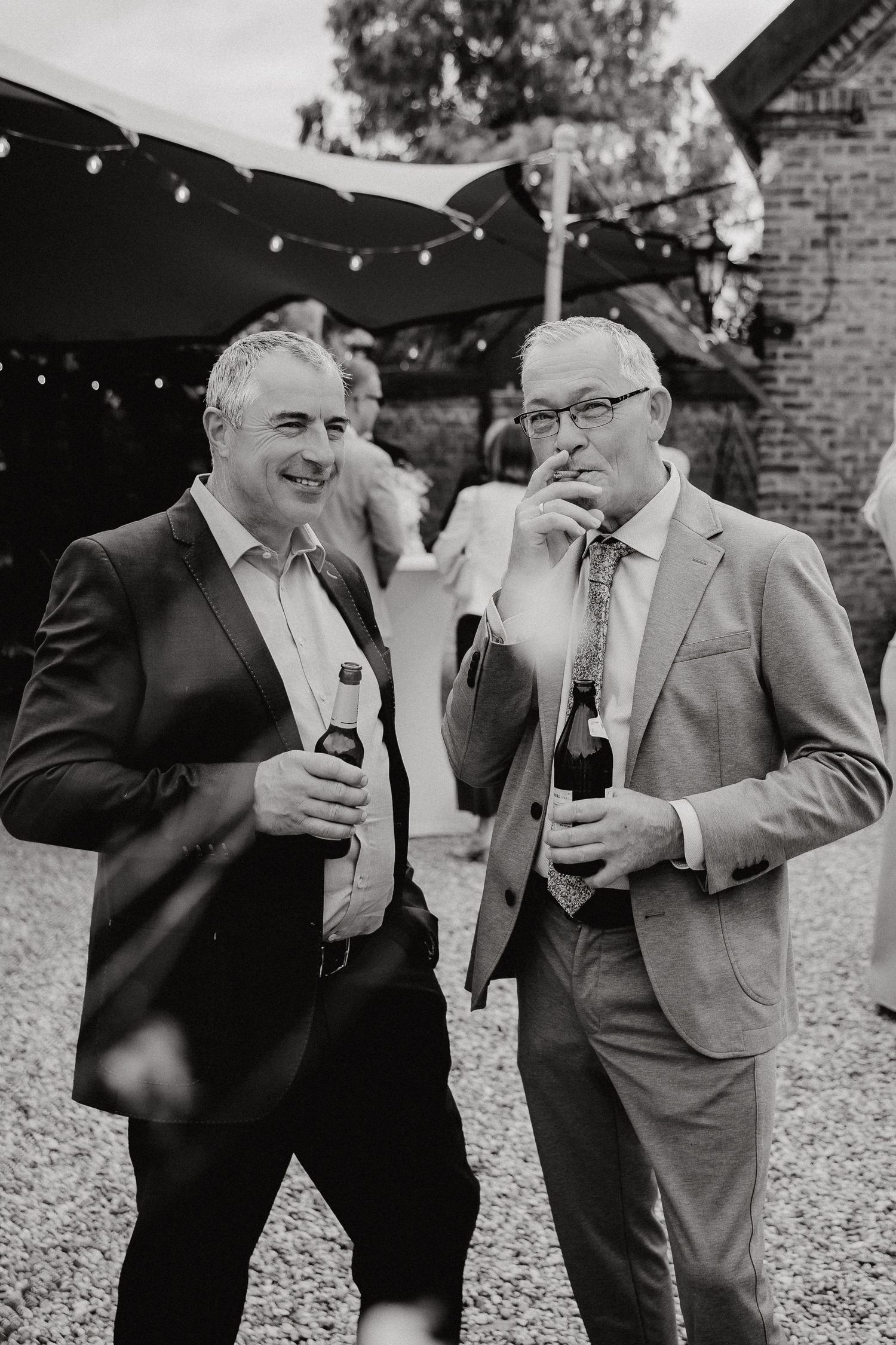Black and white photo of groomsmen in suits sharing drinks and laughs.