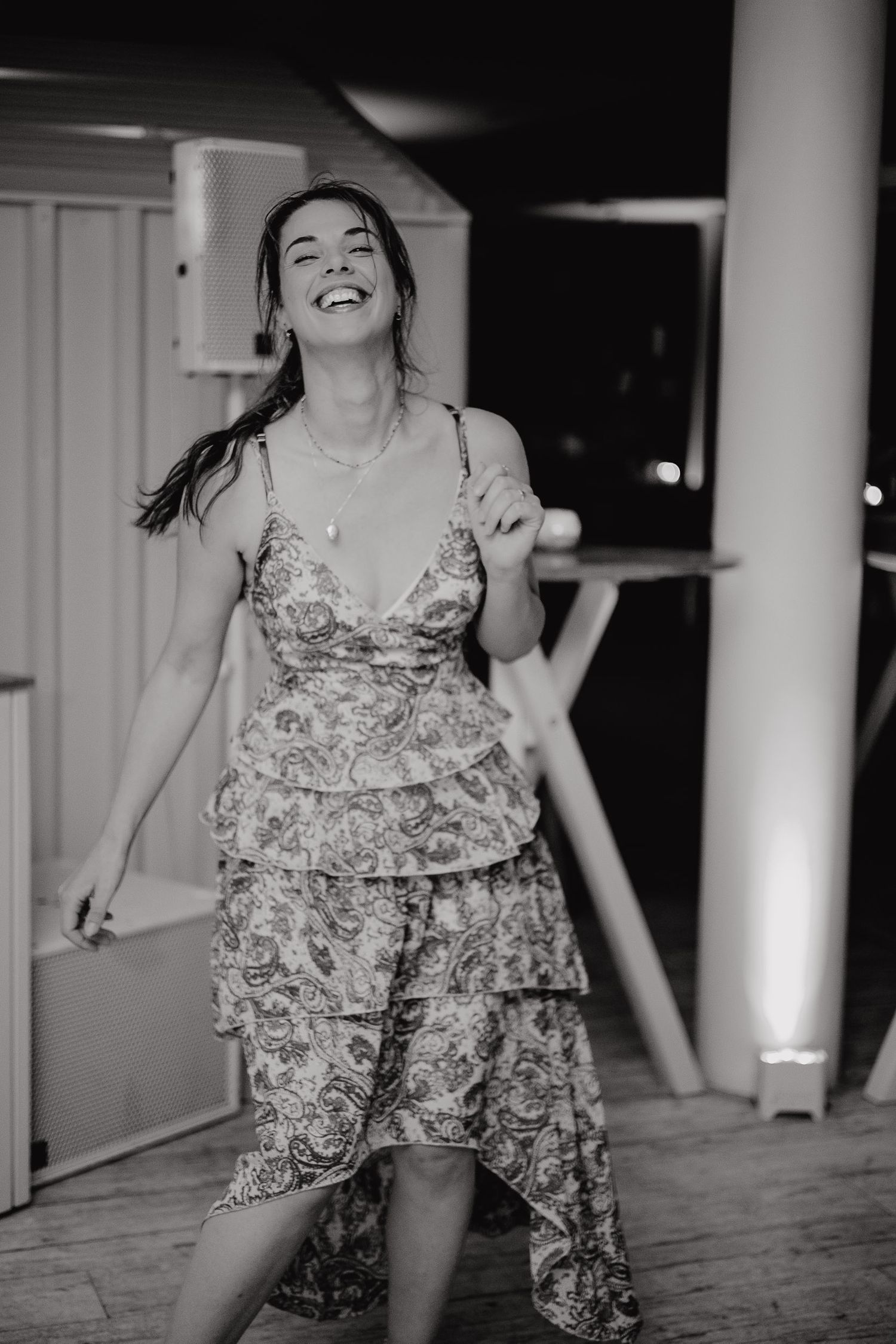 A person in a floral romper dances joyfully between white columns at night.